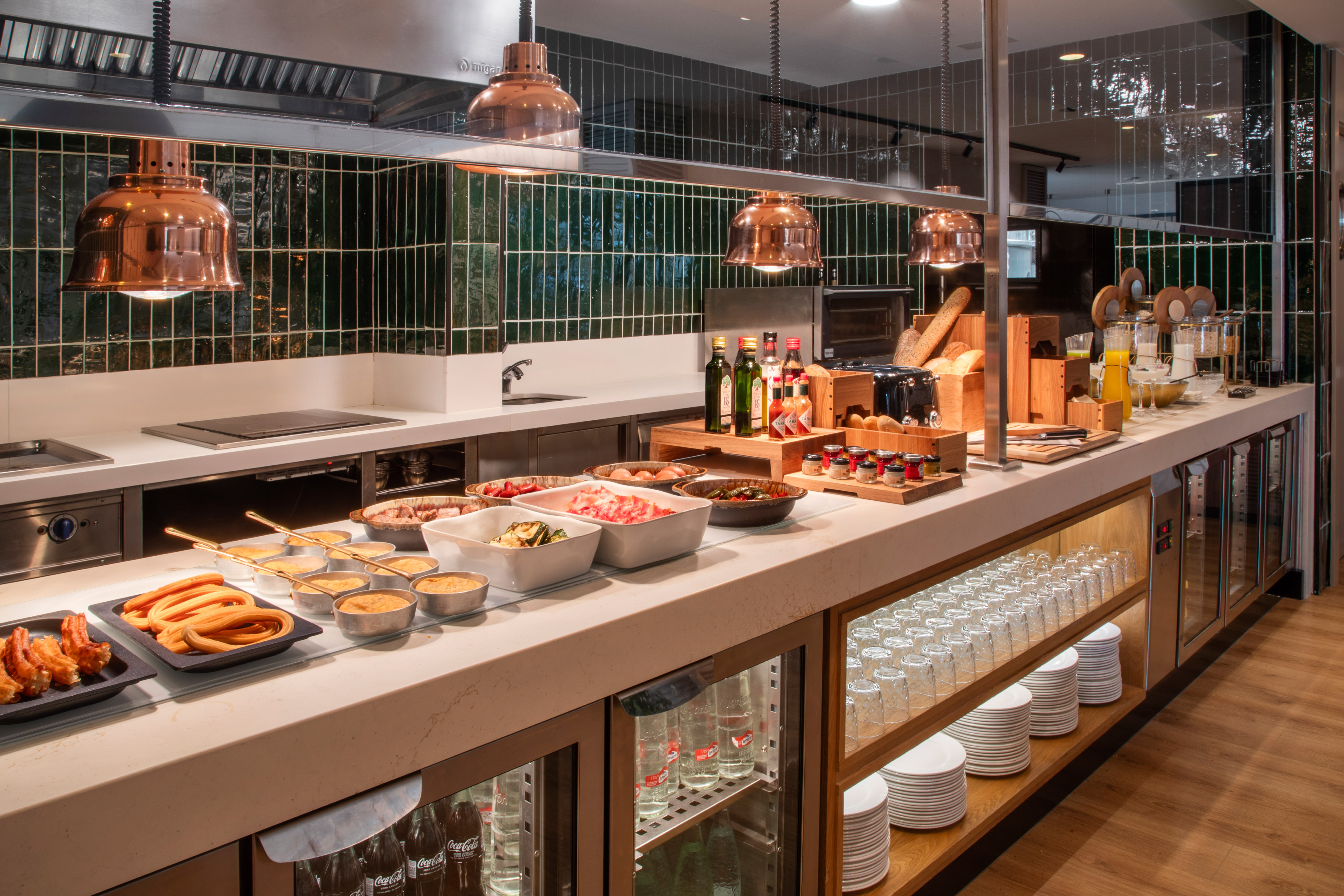 Breakfast buffet counter with churros, bacon, eggs, bread, jams, and juices.