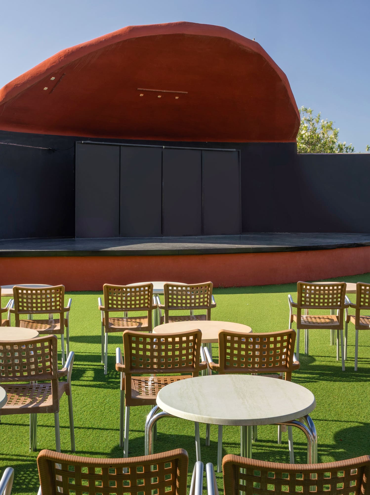 Outdoor amphitheater stage with tables, chairs on green turf, and ocean view.