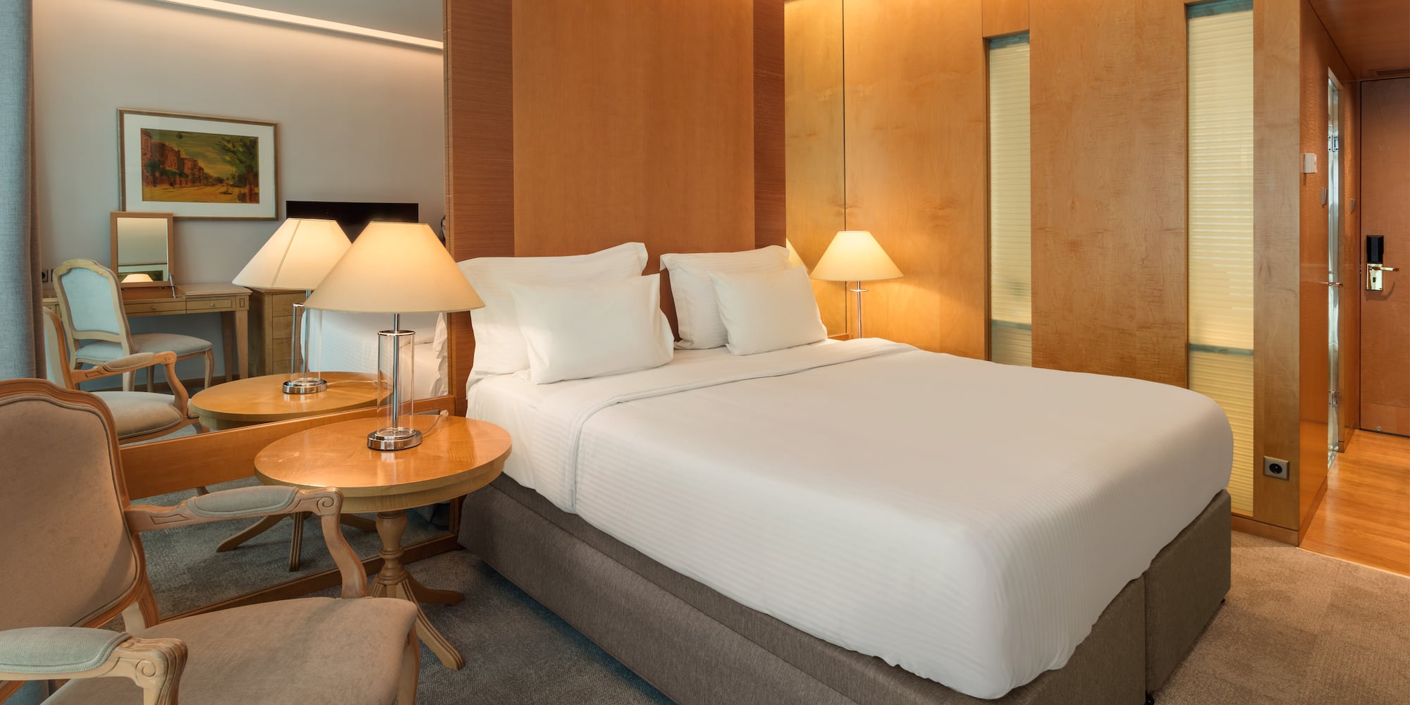 Elegant hotel bedroom with king bed, wooden accents, and soft, warm lighting.