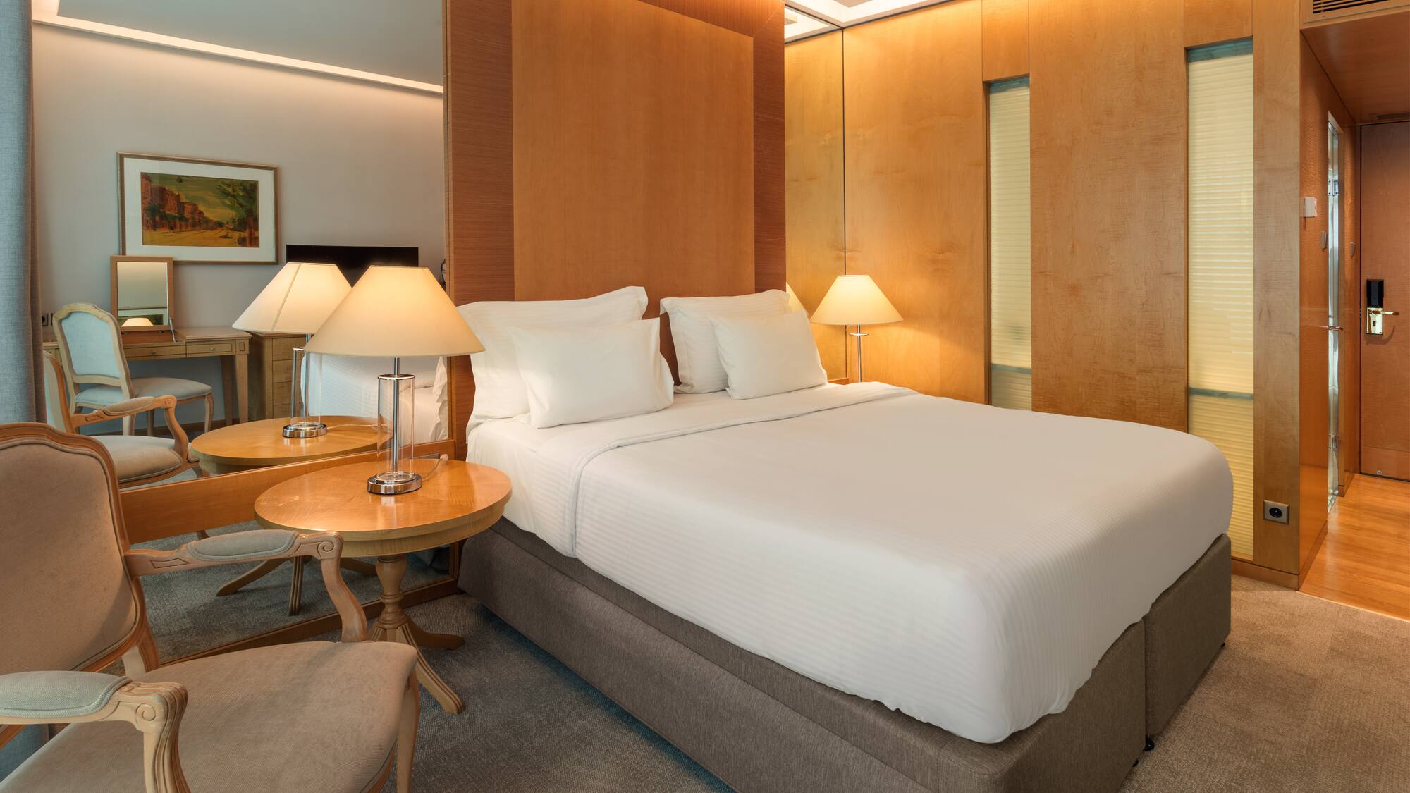 Elegant hotel bedroom with king bed, wooden accents, and soft, warm lighting.