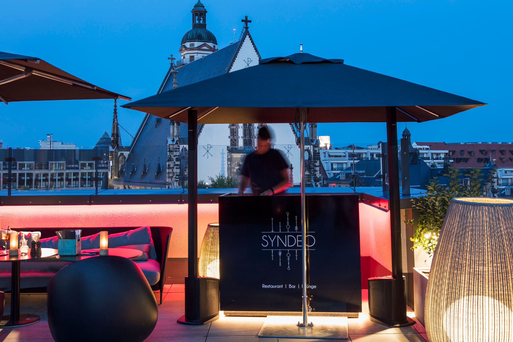 Syndeo rooftop bar/lounge, DJ, city view with church, evening ambiance.