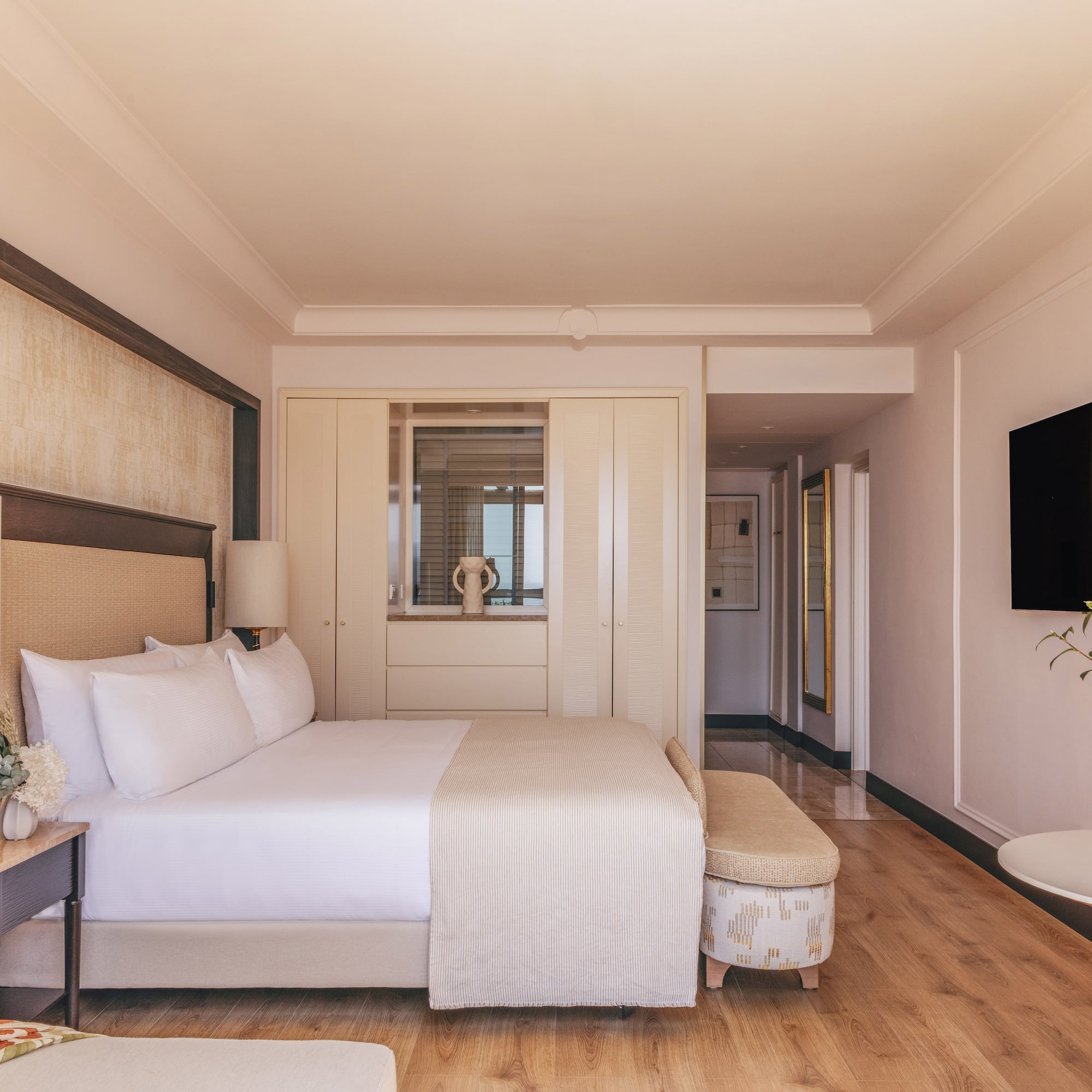 Elegant hotel bedroom with king bed, modern decor, TV, and wood floor.