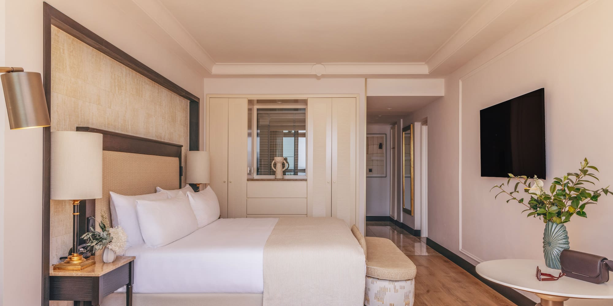 Elegant hotel bedroom with king bed, modern decor, TV, and wood floor.