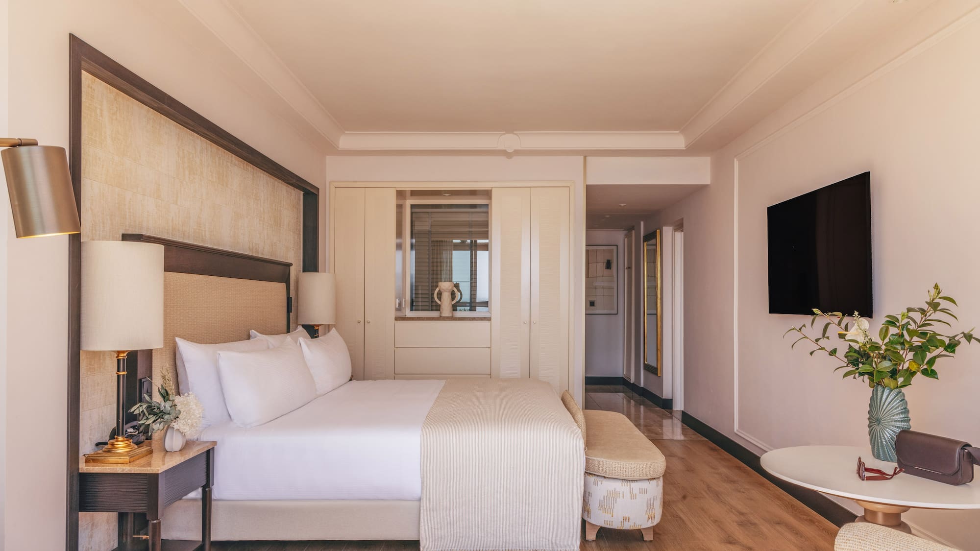 Elegant hotel bedroom with king bed, modern decor, TV, and wood floor.