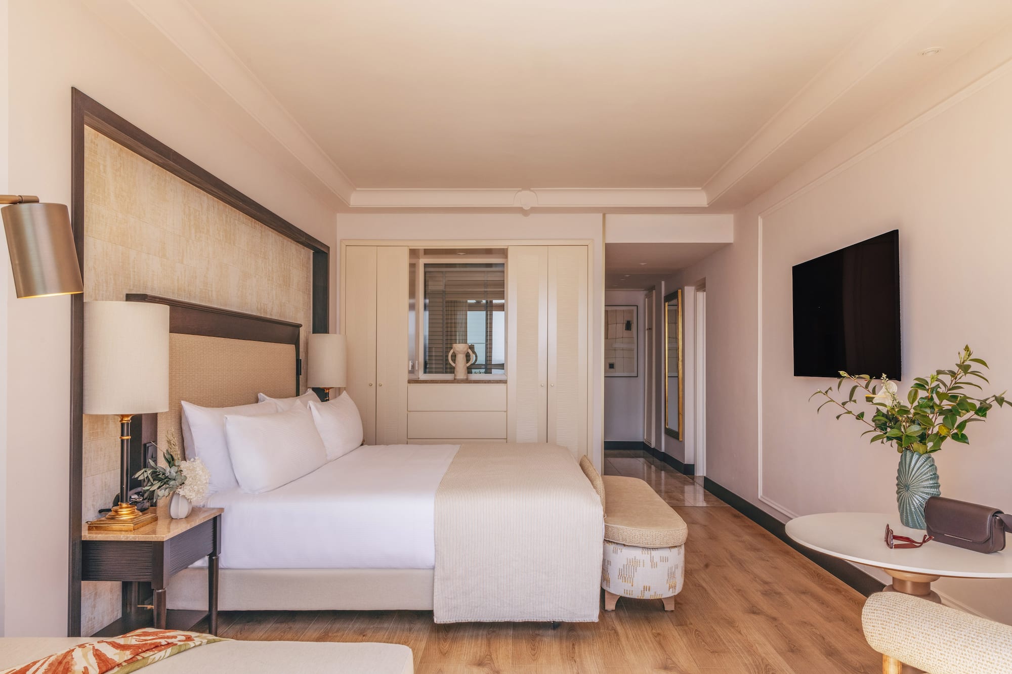 Elegant hotel bedroom with king bed, modern decor, TV, and wood floor.
