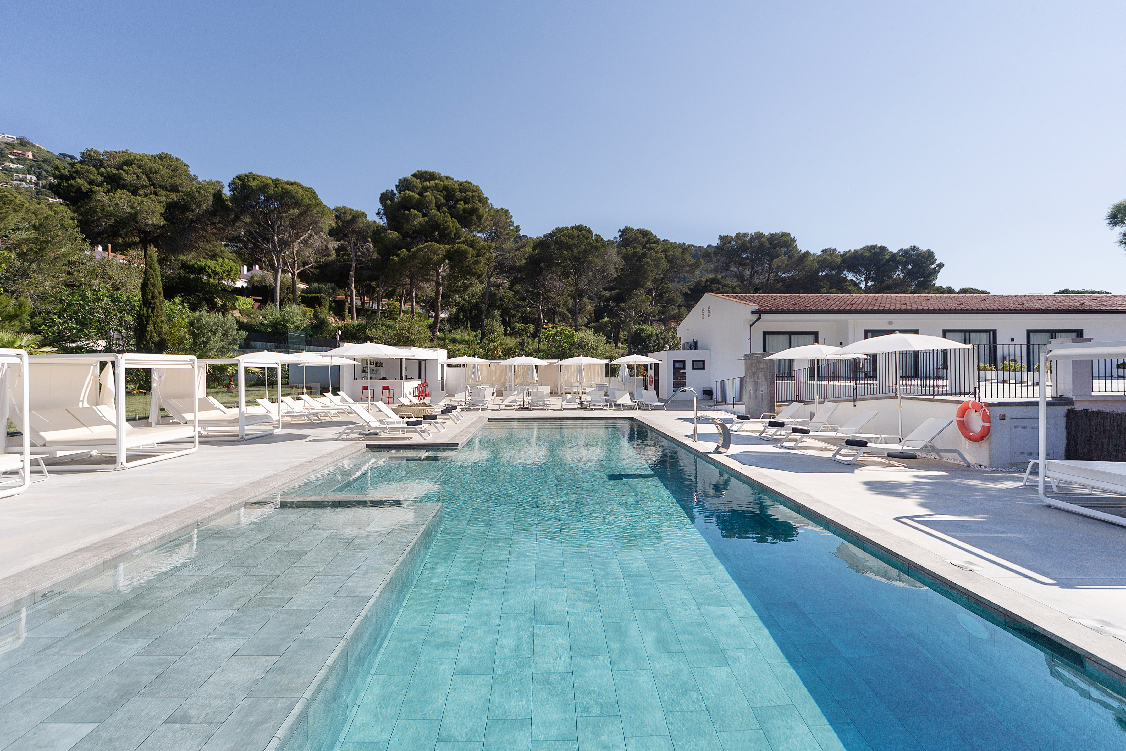 Sunny hotel swimming pool with white cabanas, loungers, and resort buildings.