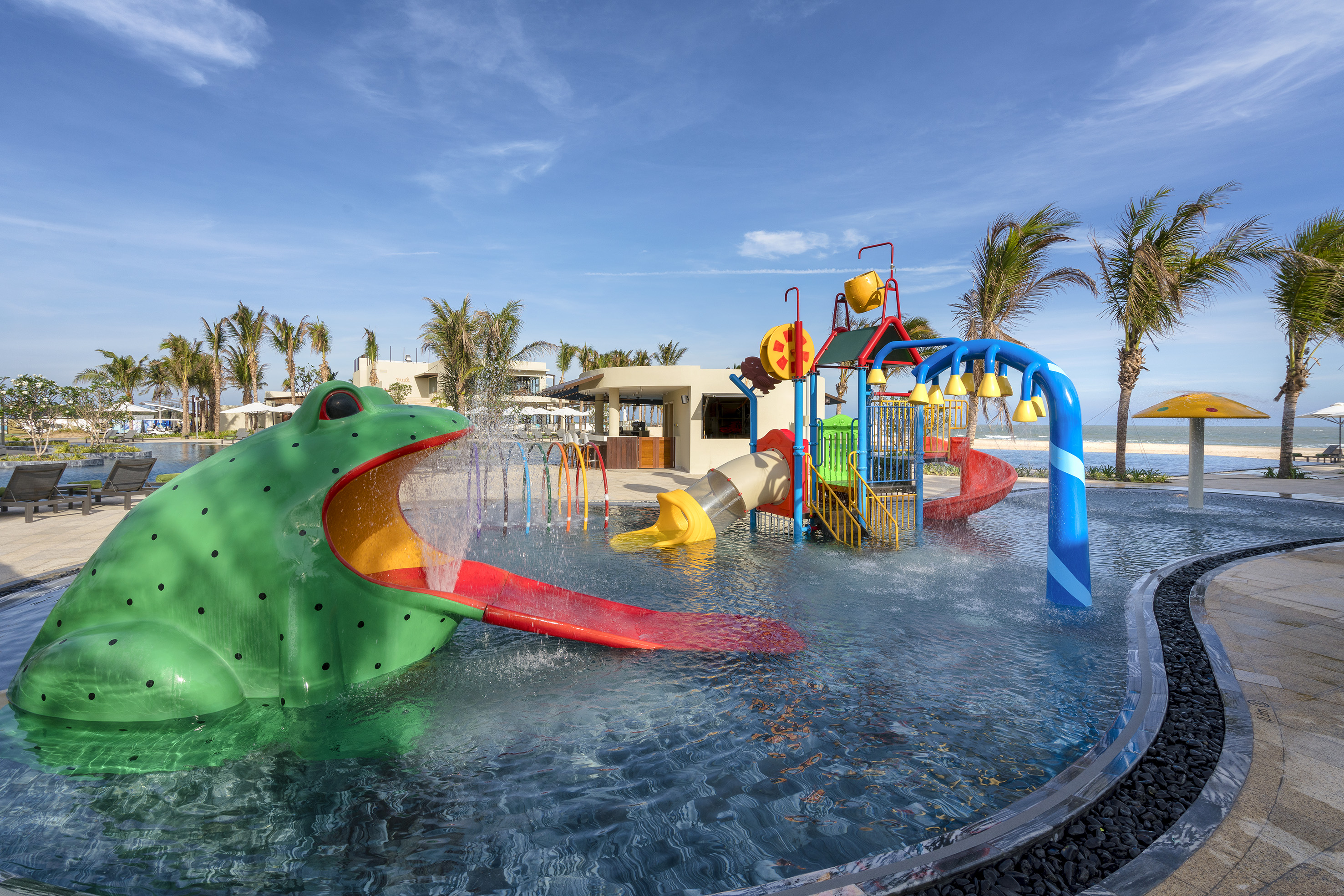 Large frog water slide and colorful splash pad at a tropical resort.