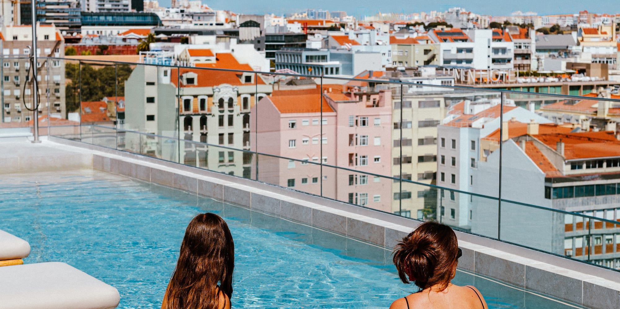 two women sitting on a pool with a city in the background