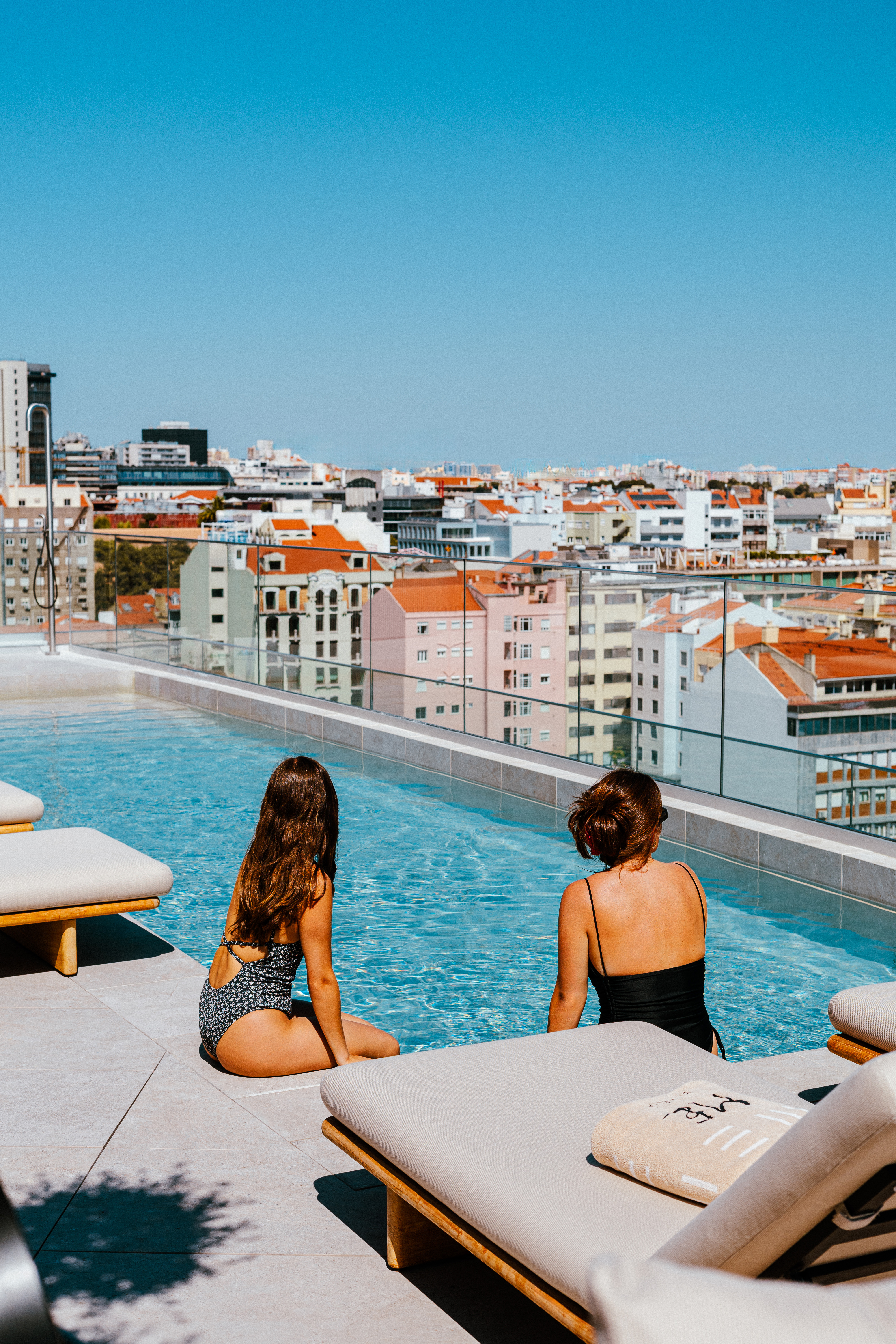 two women sitting on a pool with a city in the background