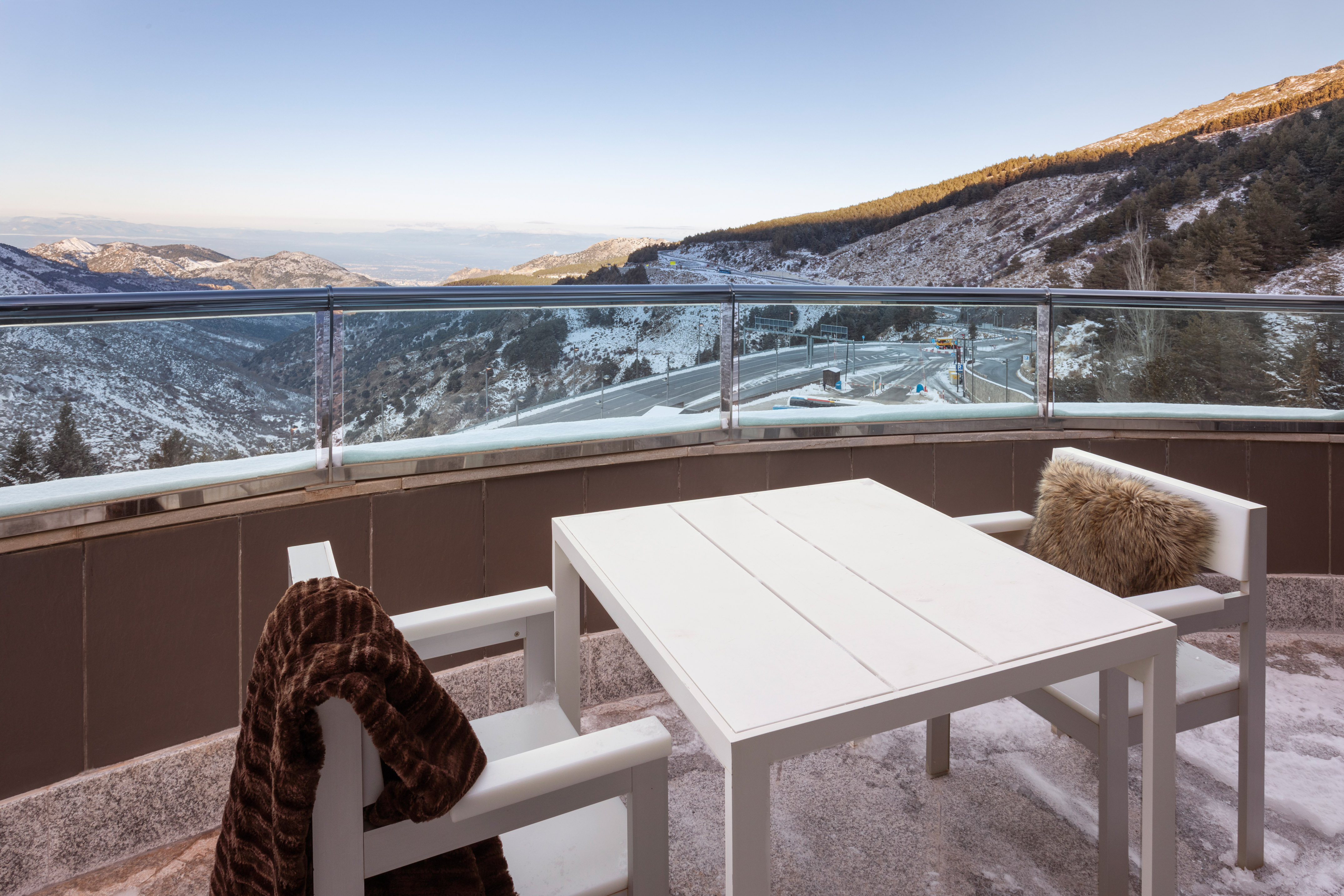 Winter balcony, white outdoor table & chairs, snowy mountain valley view.