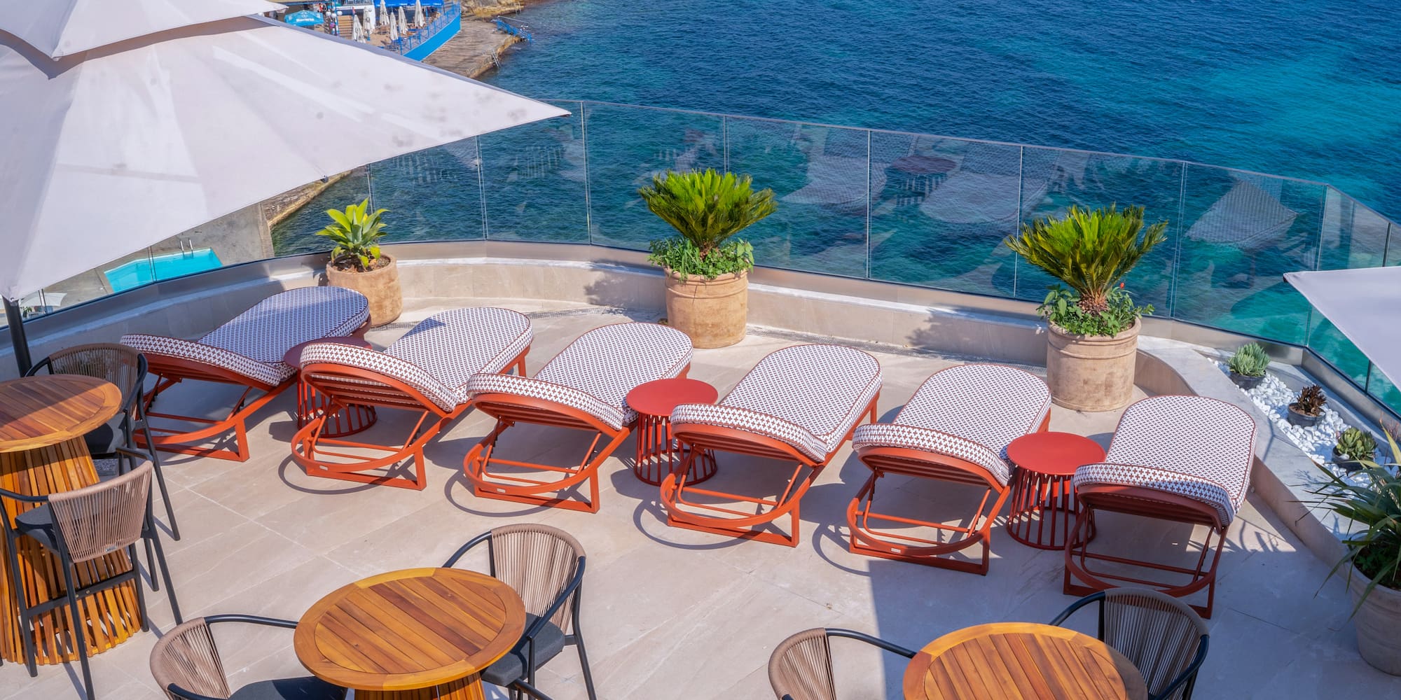Hotel rooftop terrace with sea view, sunbeds, and outdoor dining tables.
