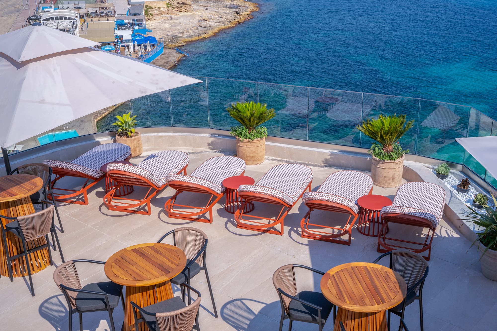 Hotel rooftop terrace with sea view, sunbeds, and outdoor dining tables.