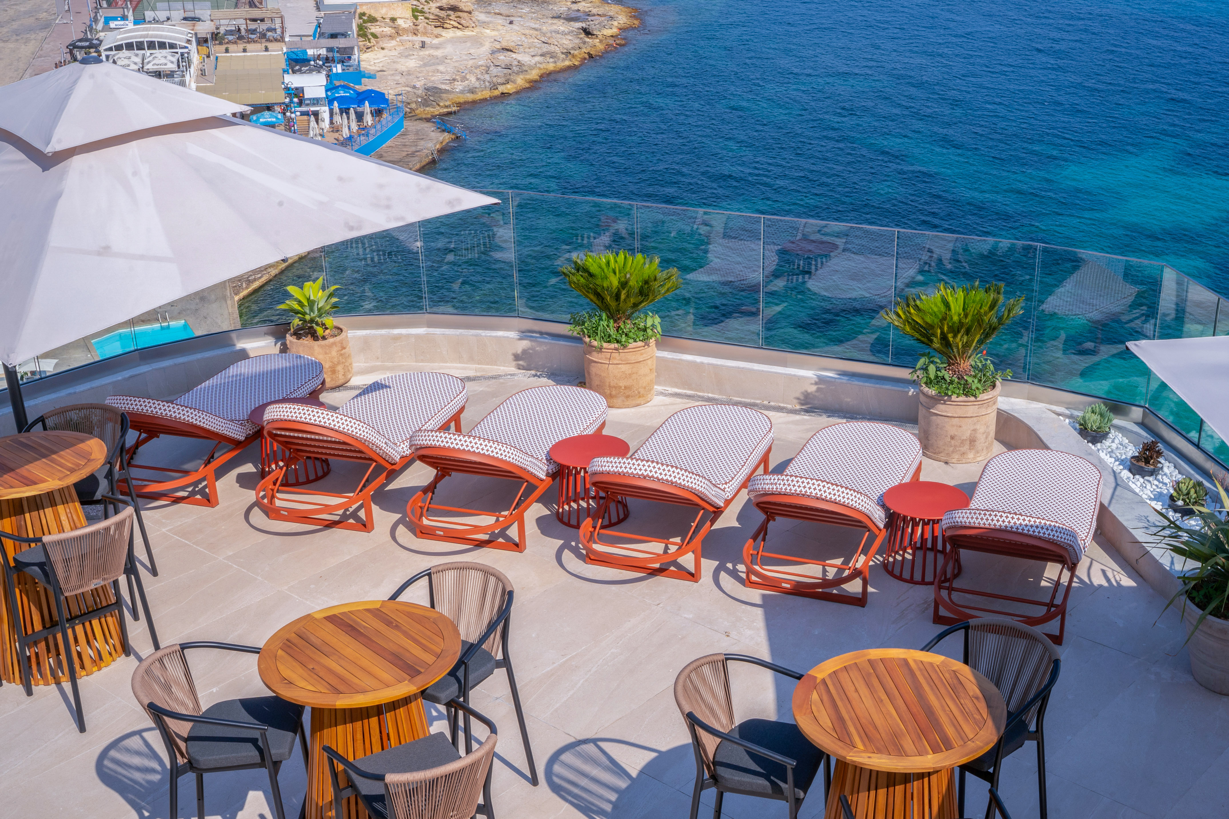Hotel rooftop terrace with sea view, sunbeds, and outdoor dining tables.