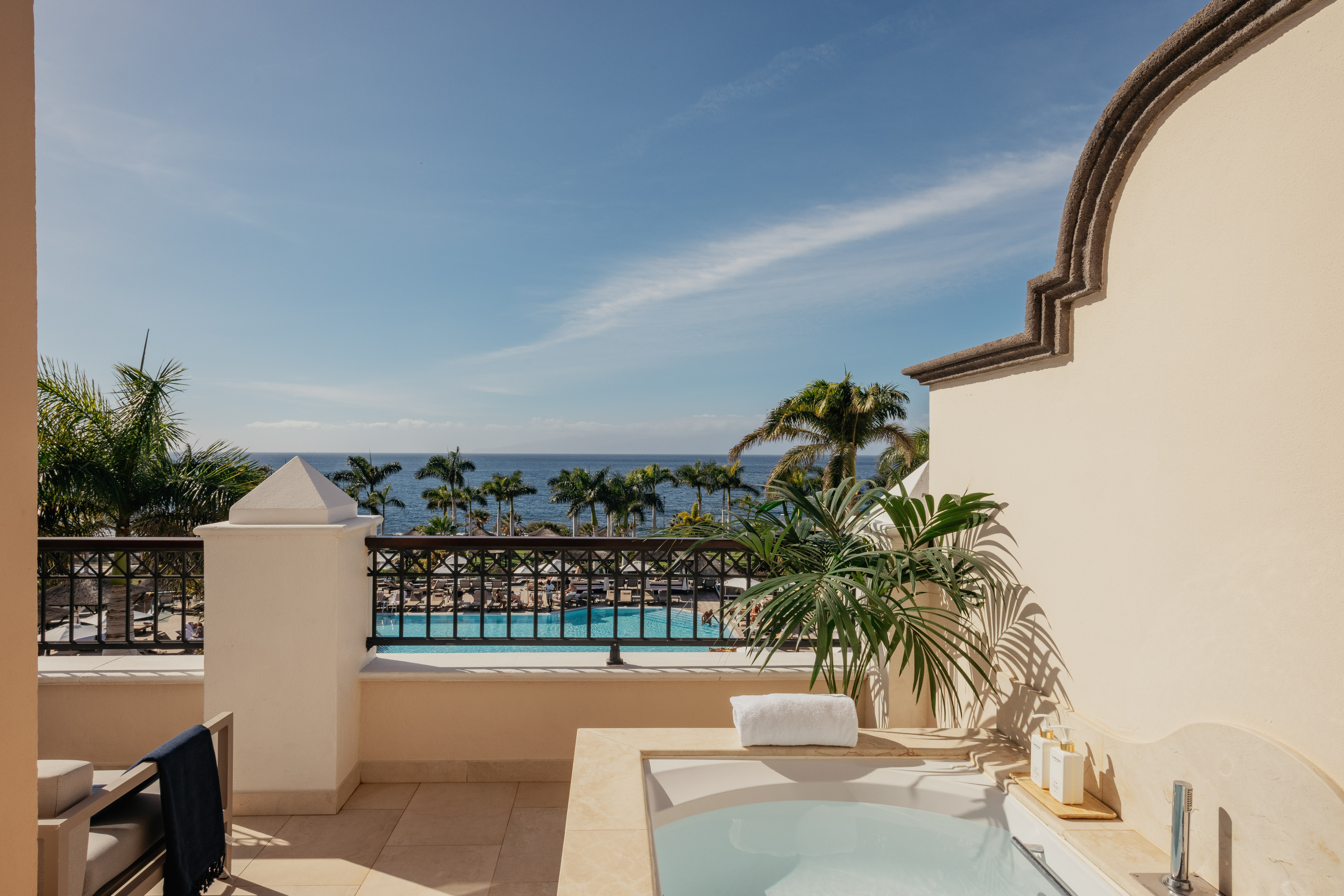 Balcony hot tub with ocean view, palm trees, and resort swimming pool.