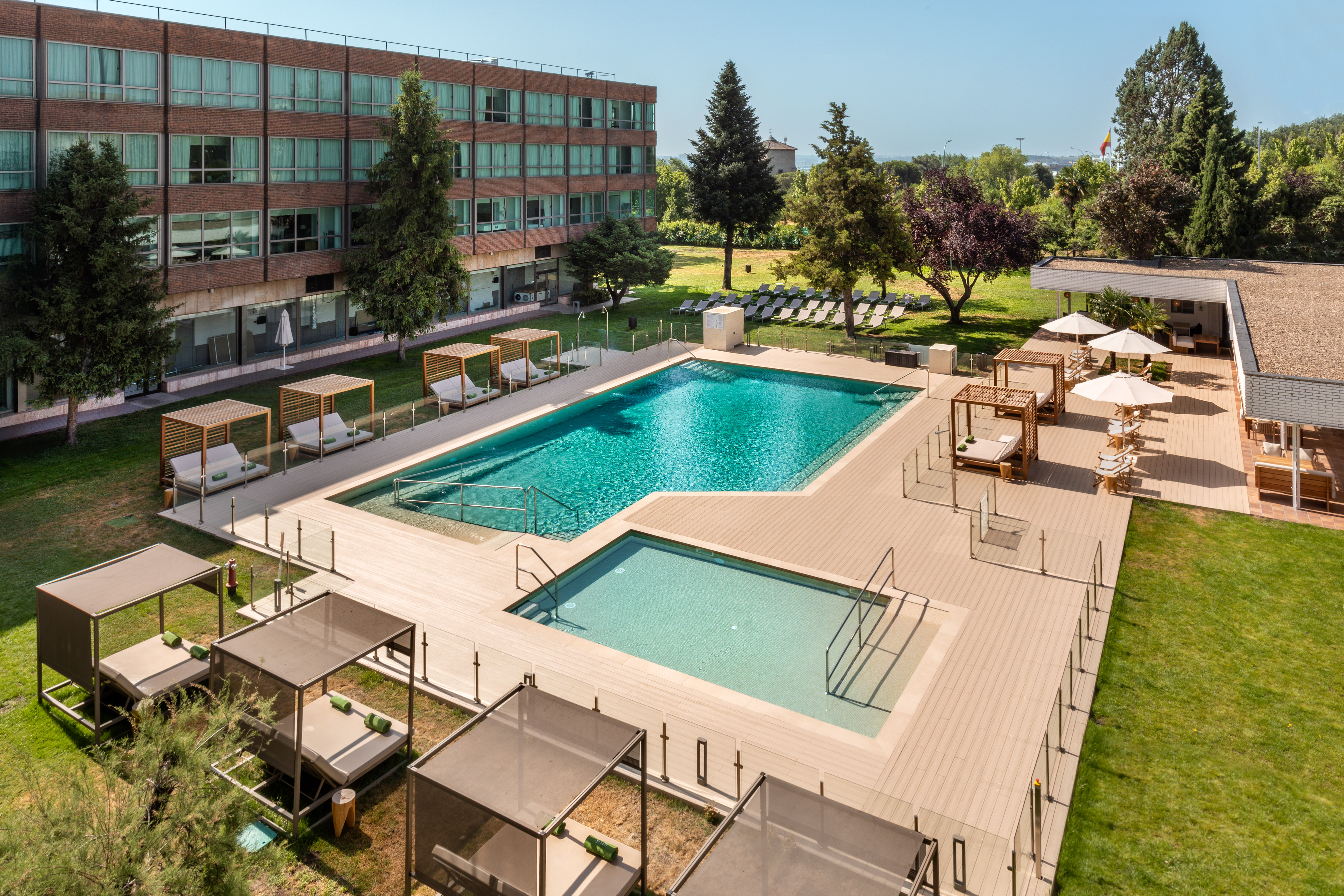 Resort outdoor swimming pool, sun deck, loungers, cabanas, and green landscape.