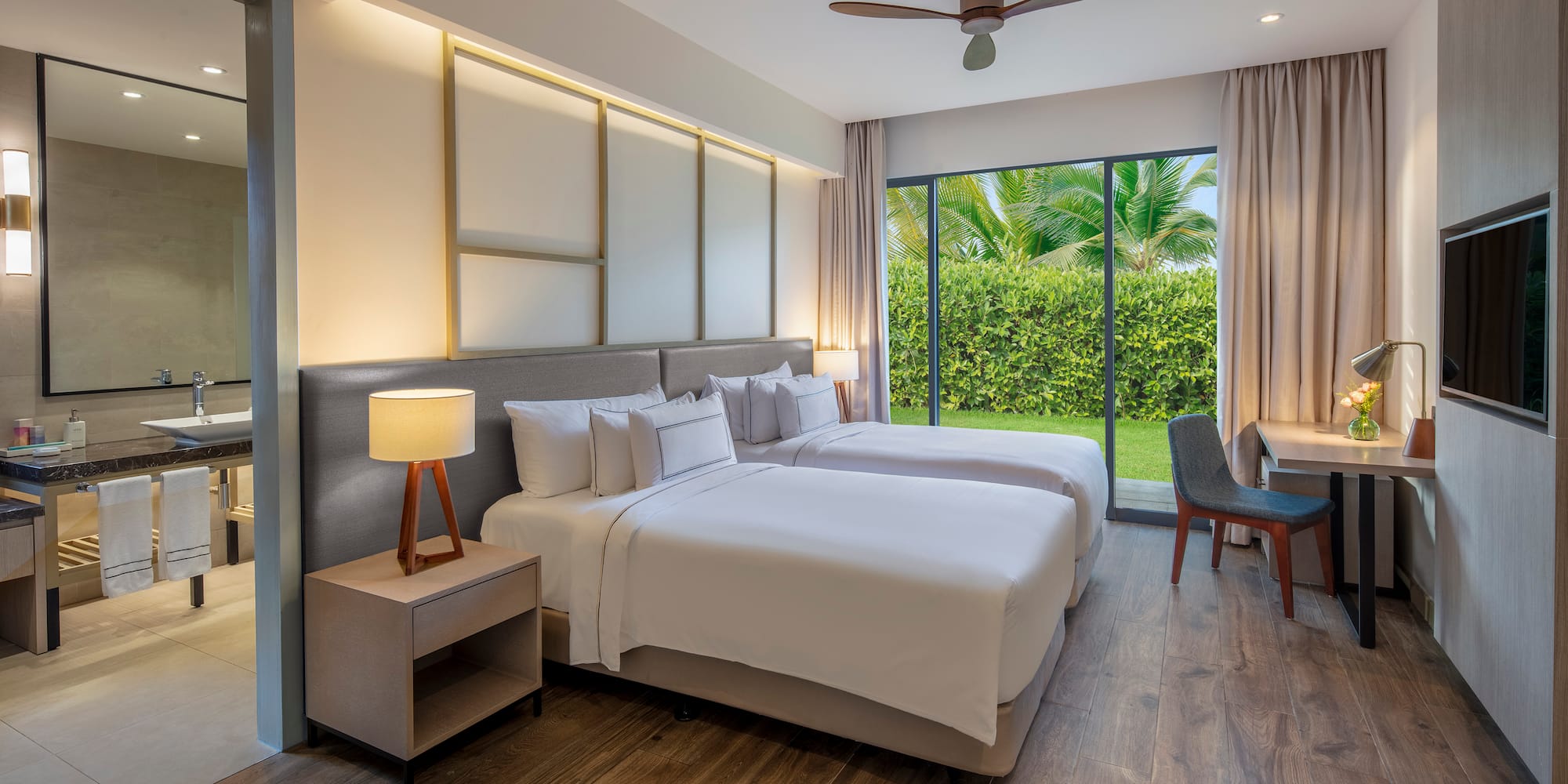 Modern hotel room with twin beds, garden view, wood floor, and desk.