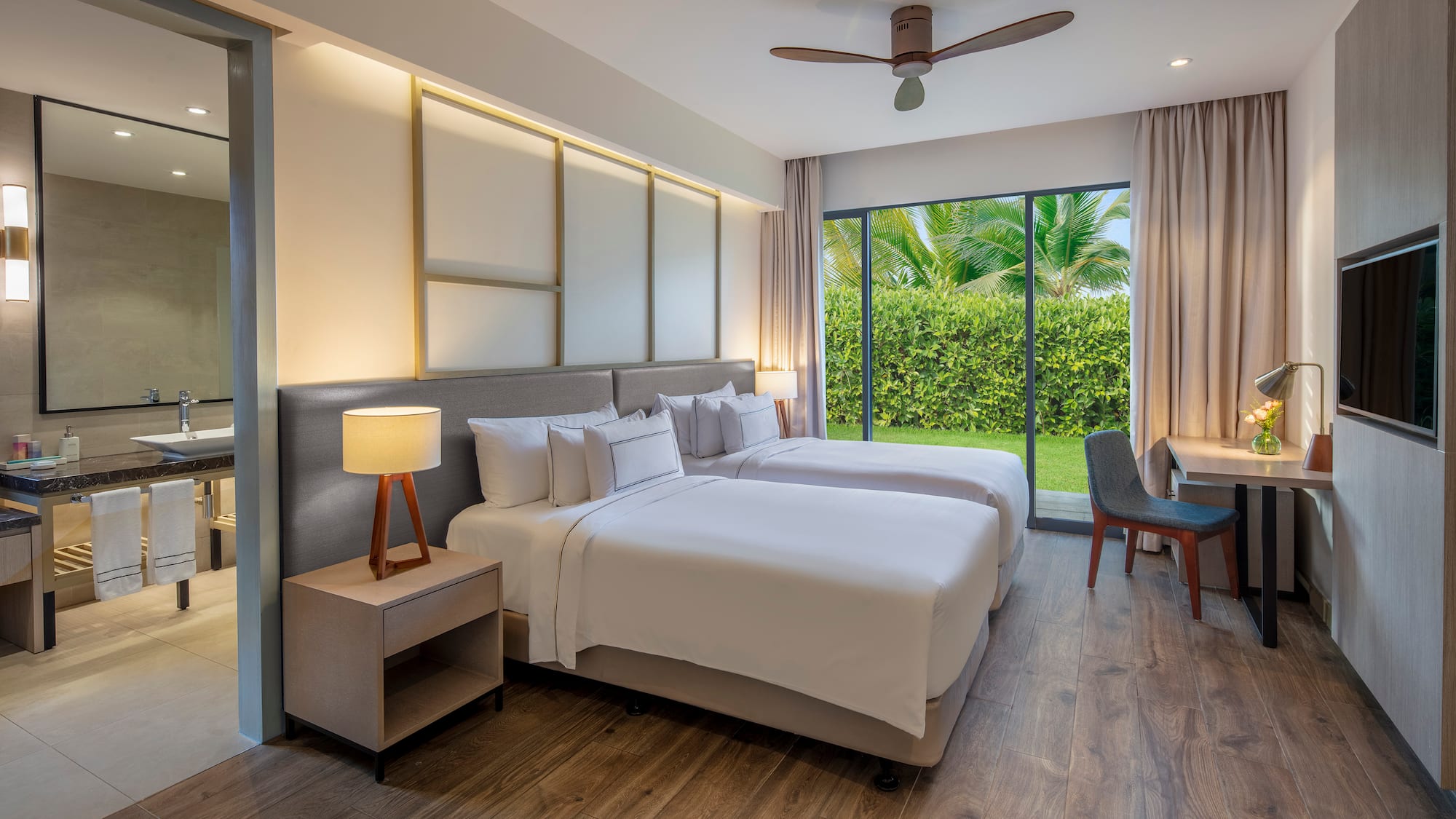 Modern hotel room with twin beds, garden view, wood floor, and desk.