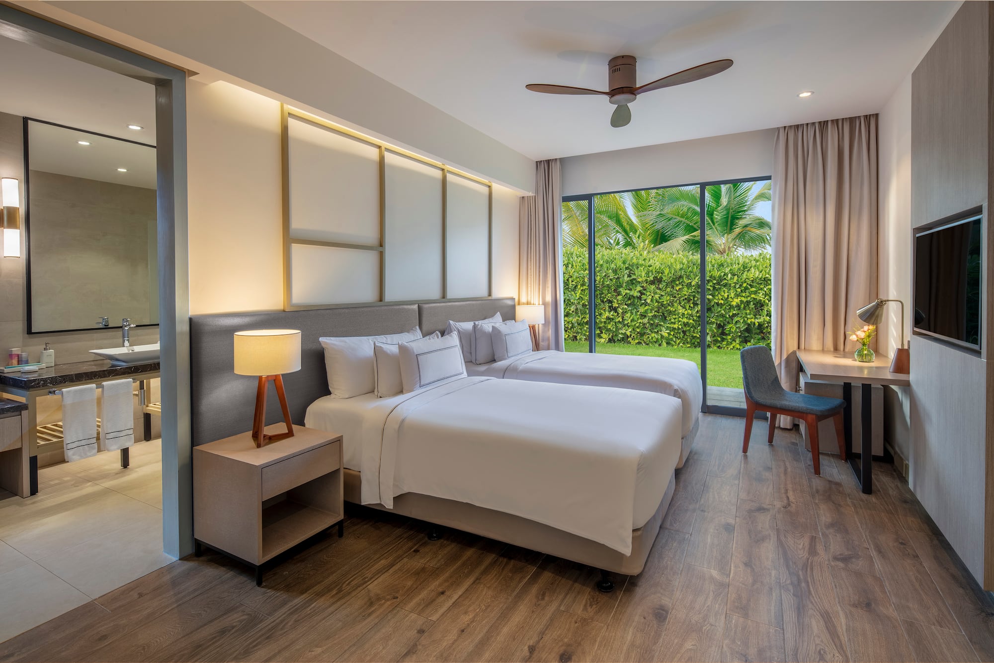 Modern hotel room with twin beds, garden view, wood floor, and desk.