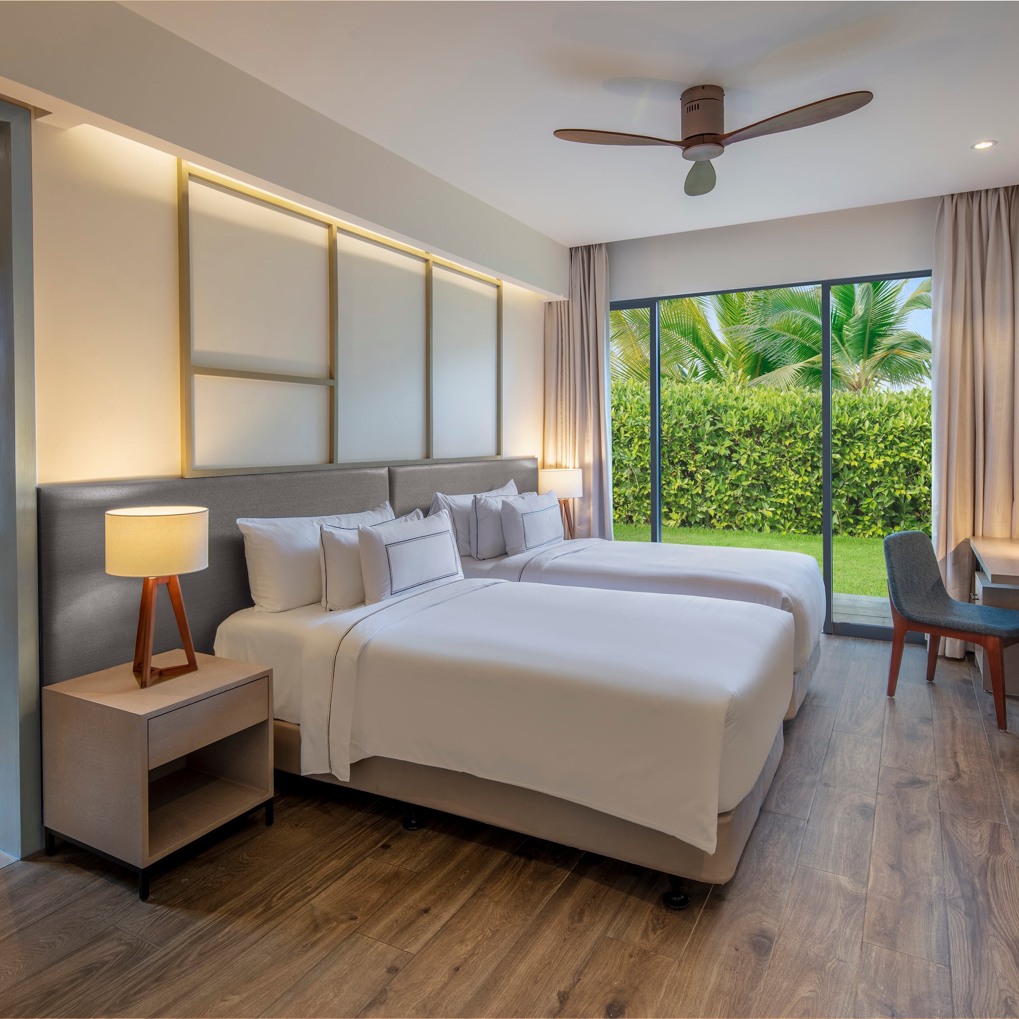 Modern hotel room with twin beds, garden view, wood floor, and desk.