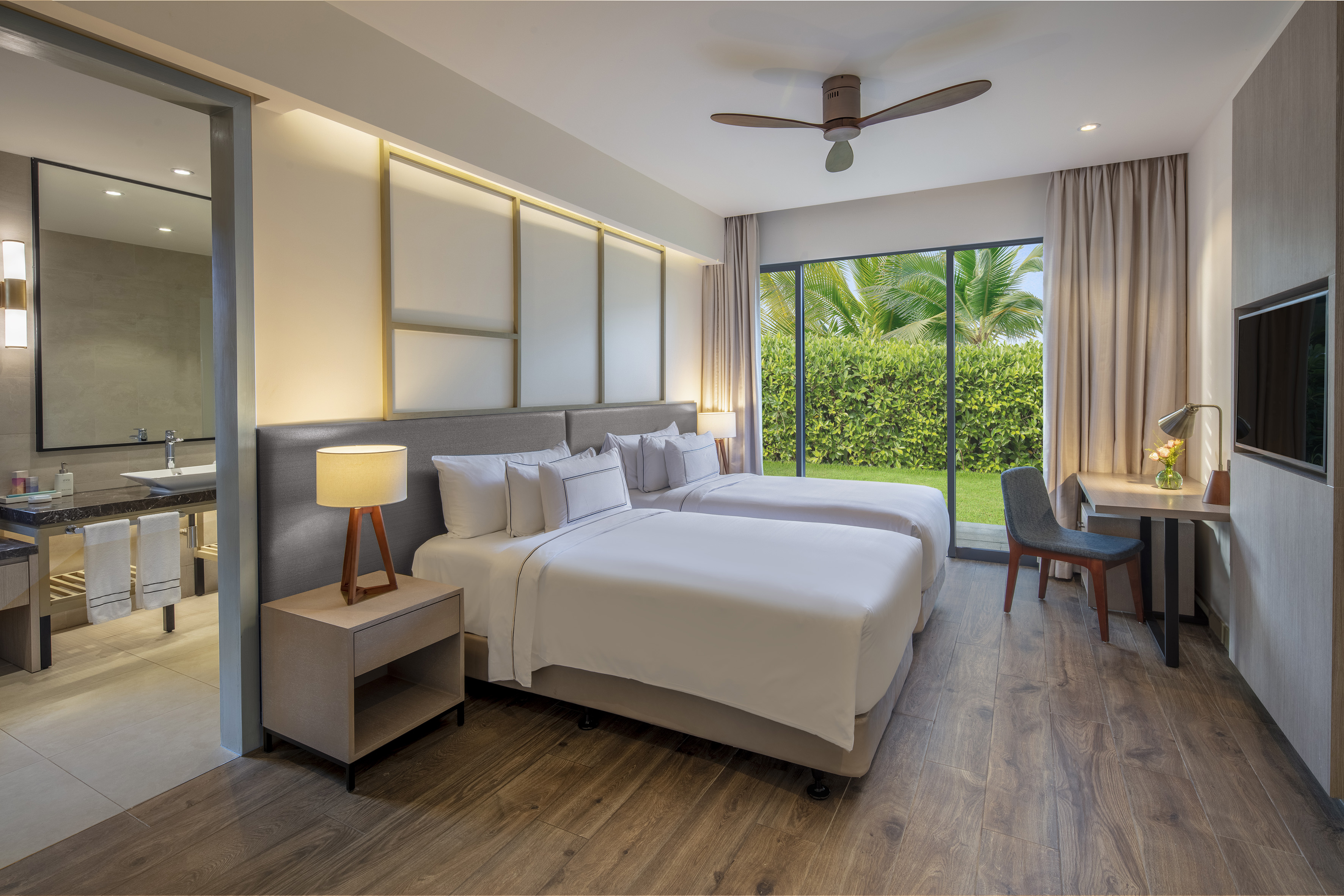 Modern hotel room with twin beds, garden view, wood floor, and desk.