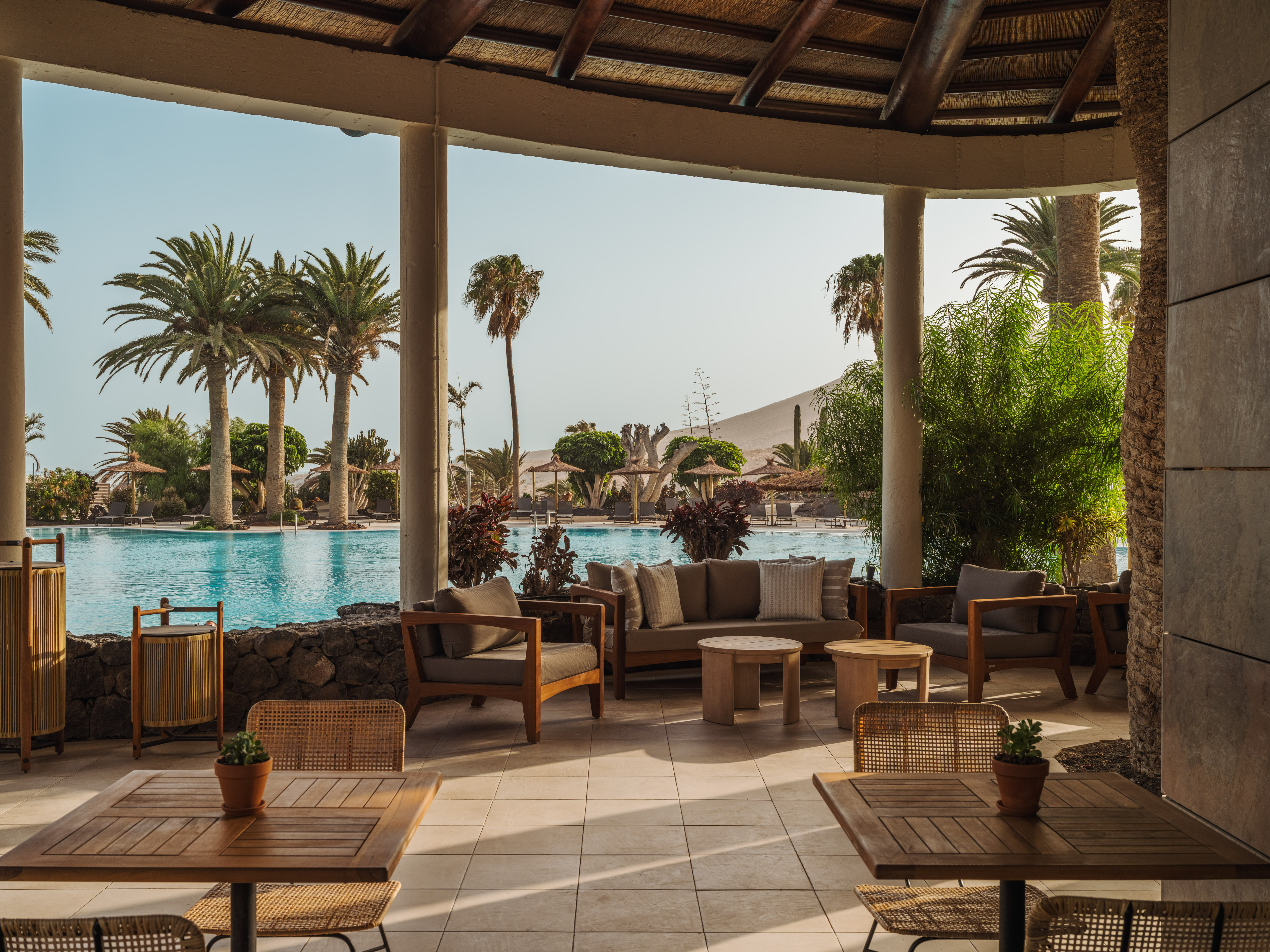 Resort terrace with pool, palm trees, desert landscape, and lounge seating.