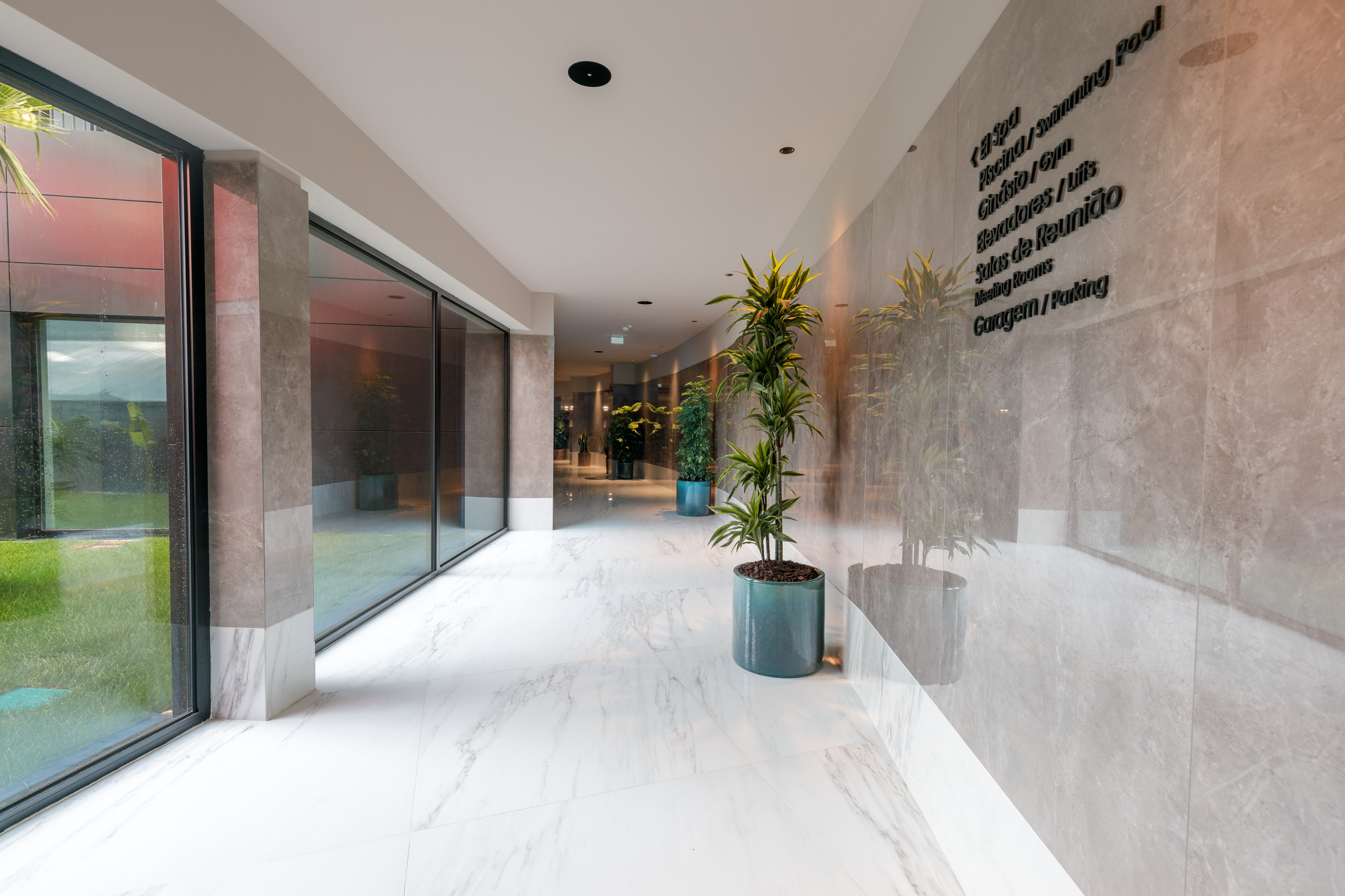 Modern hotel hallway with white marble floor, glass facade, and amenity signage.