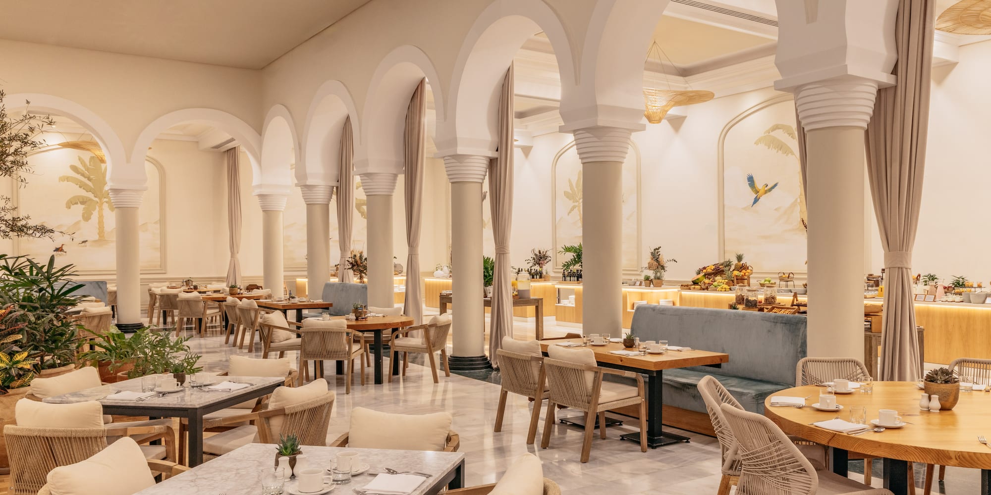 Elegant restaurant with archways, tropical murals, dining tables, and buffet.