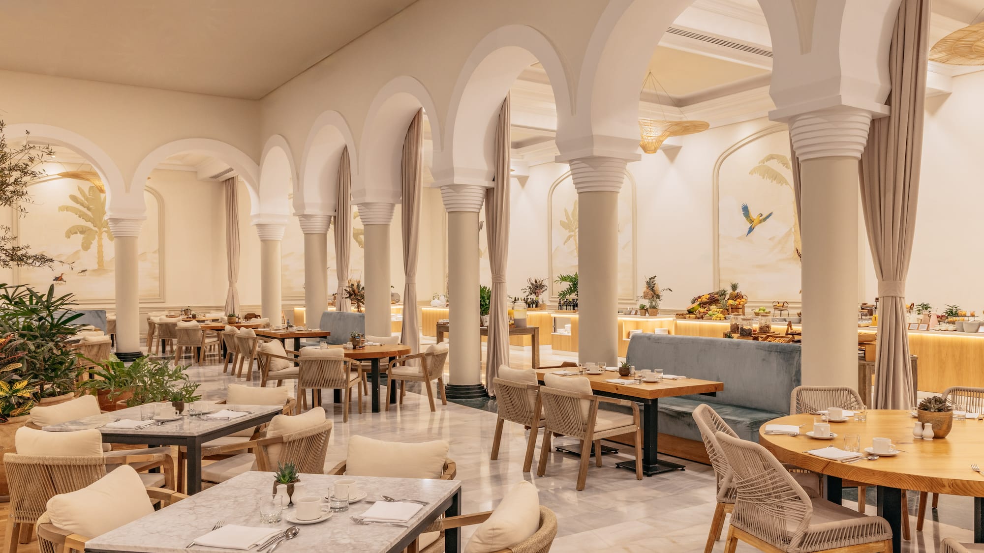 Elegant restaurant with archways, tropical murals, dining tables, and buffet.