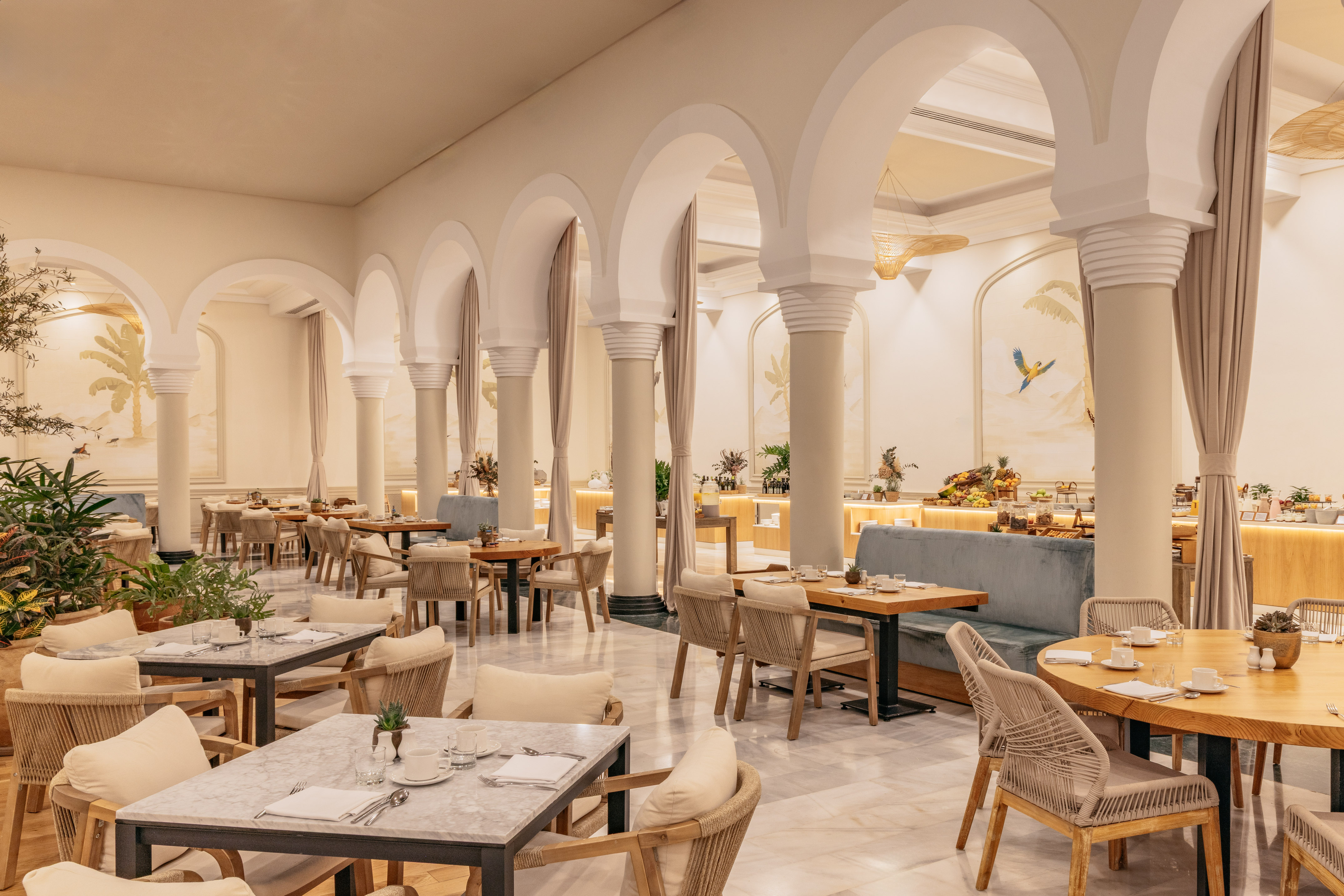 Elegant restaurant with archways, tropical murals, dining tables, and buffet.