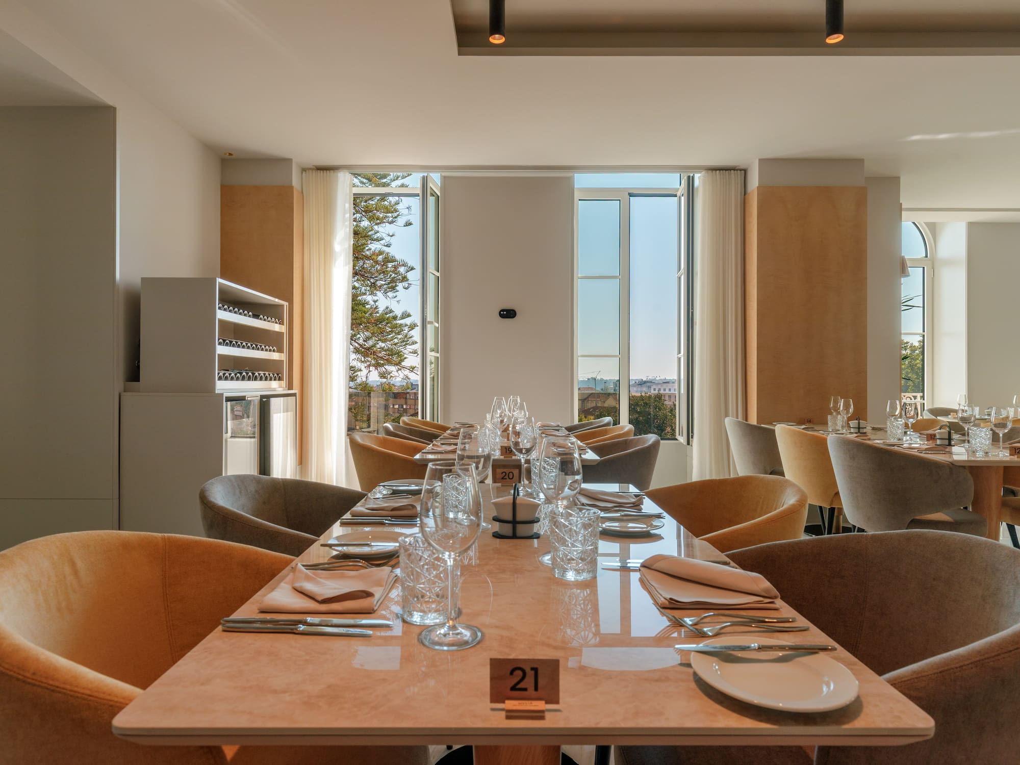 Elegant restaurant dining room, set tables, plush chairs, city view.