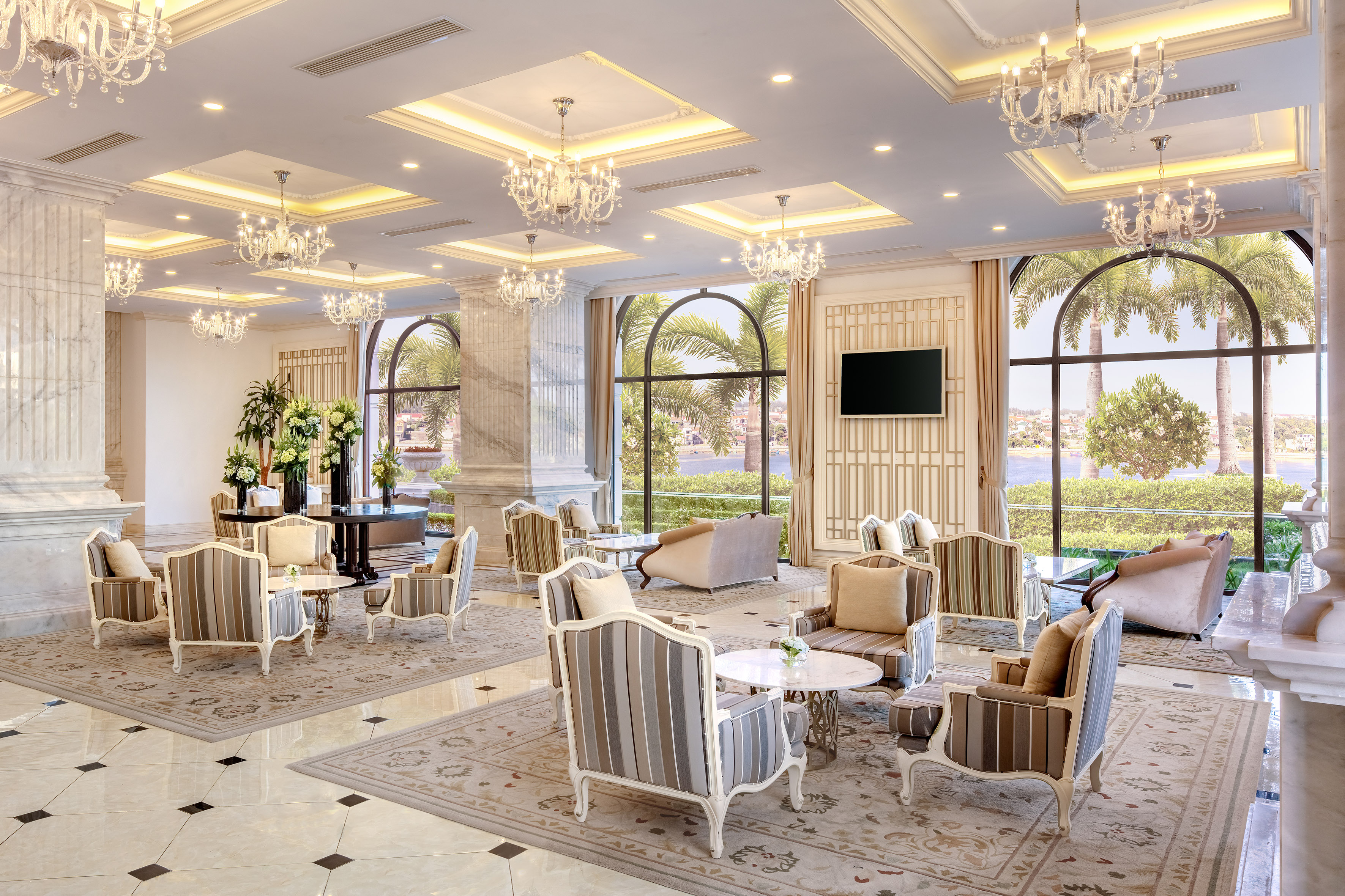 Luxury hotel lobby with elegant seating, chandeliers, and waterfront view.