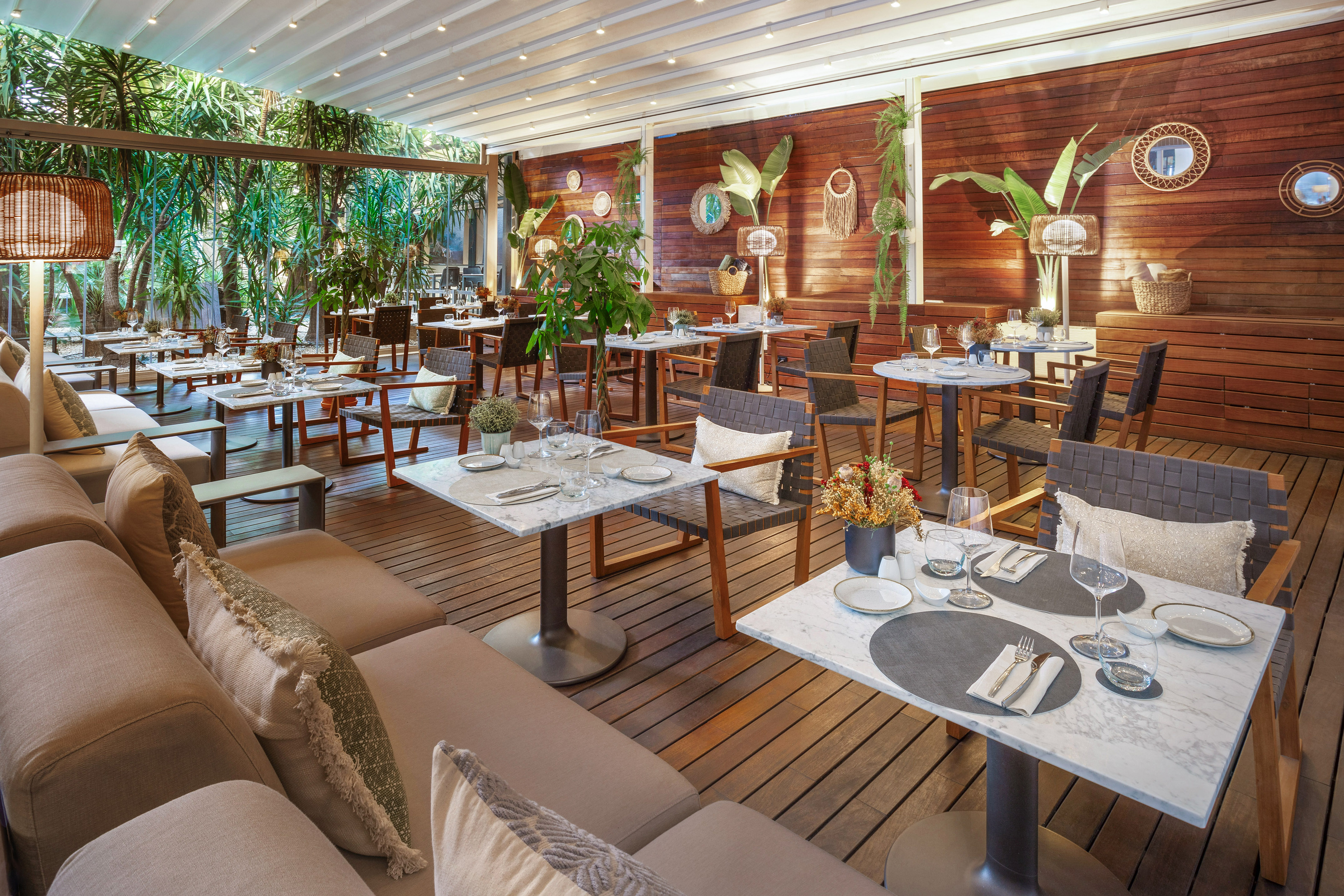 Elegant restaurant patio with marble tables, wood walls, and lush tropical plants.