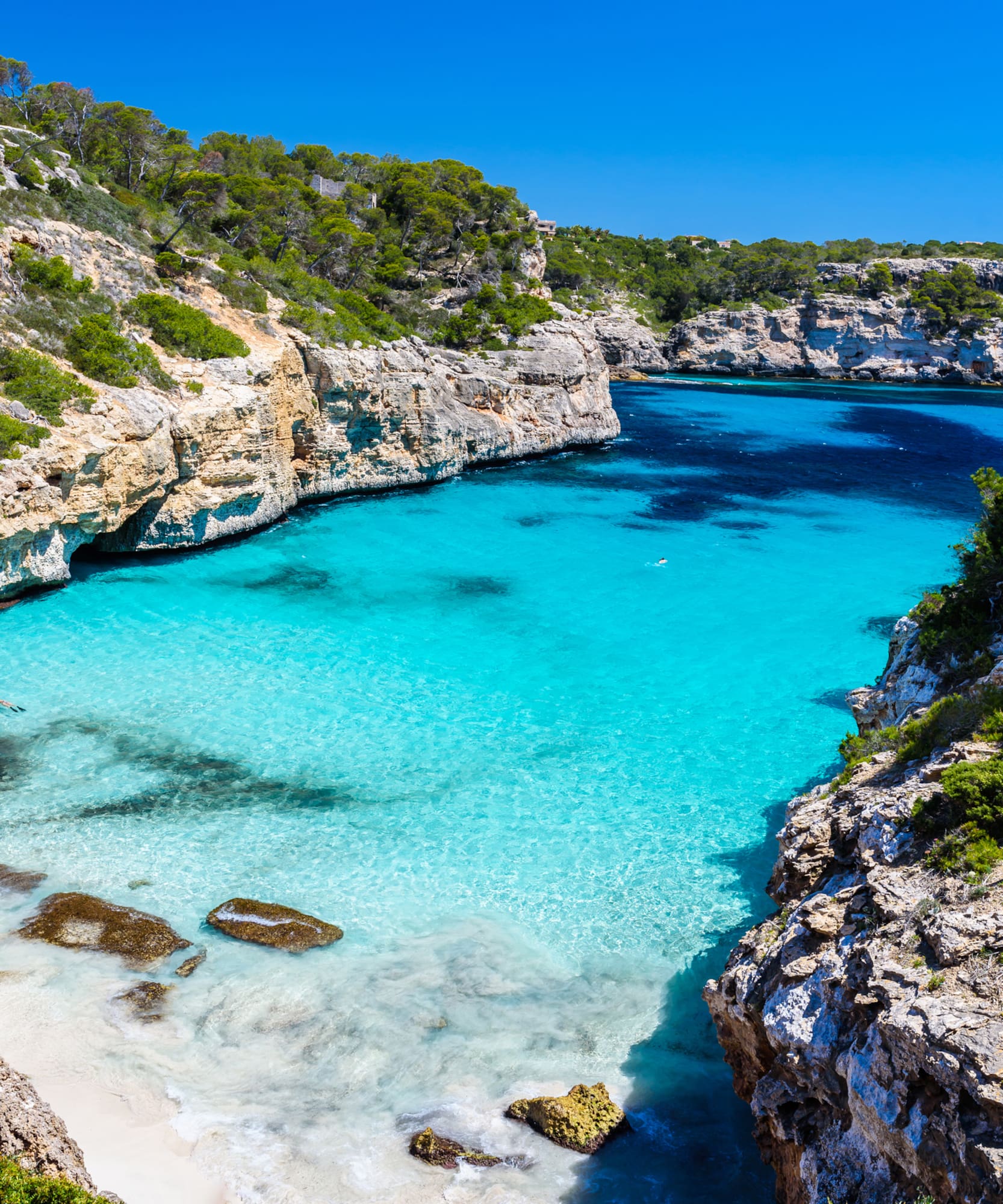 Cala turquesa en Mallorca entre acantilados rocosos y playa de arena.