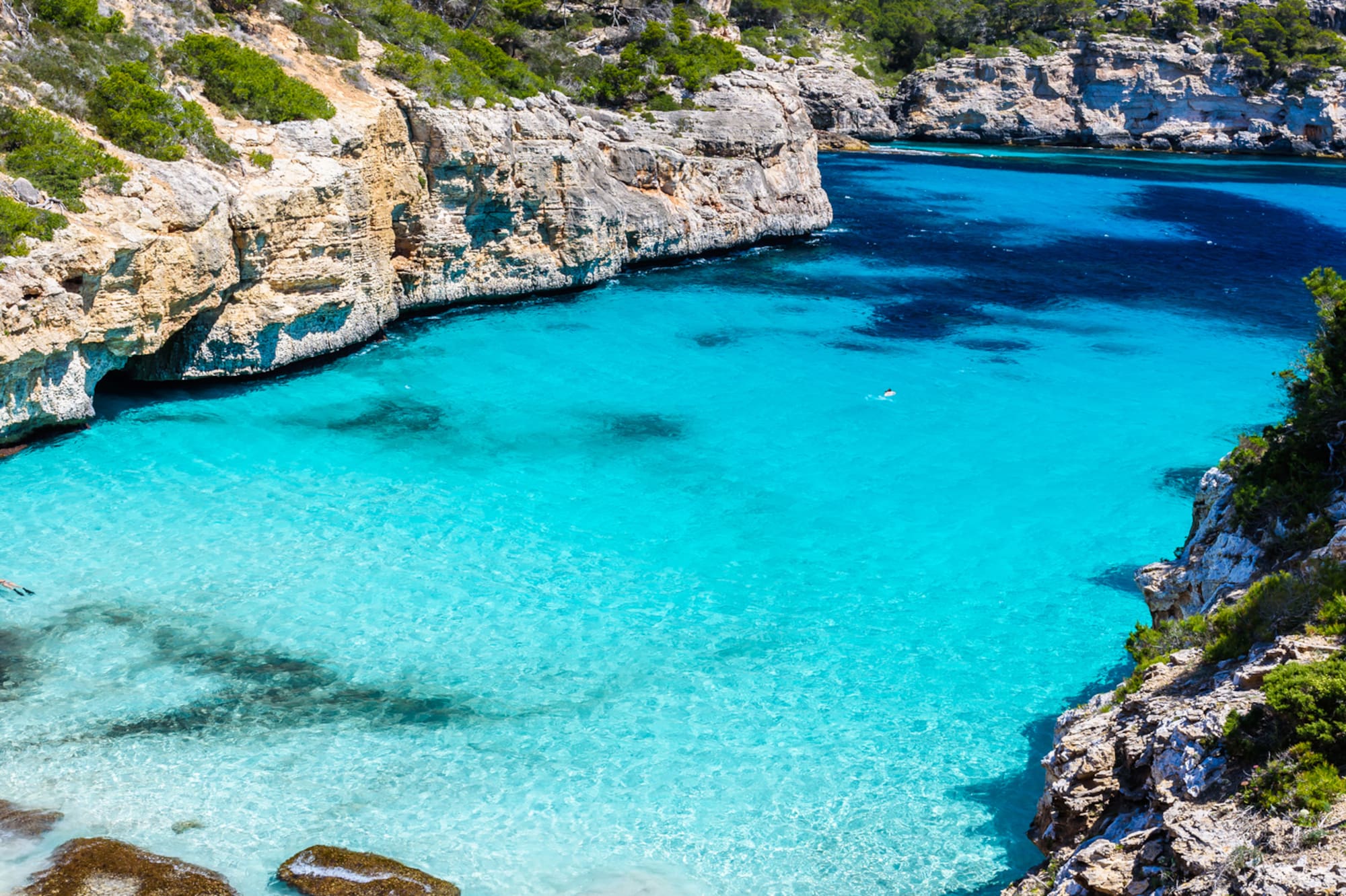 Cala turquesa en Mallorca entre acantilados rocosos y playa de arena.