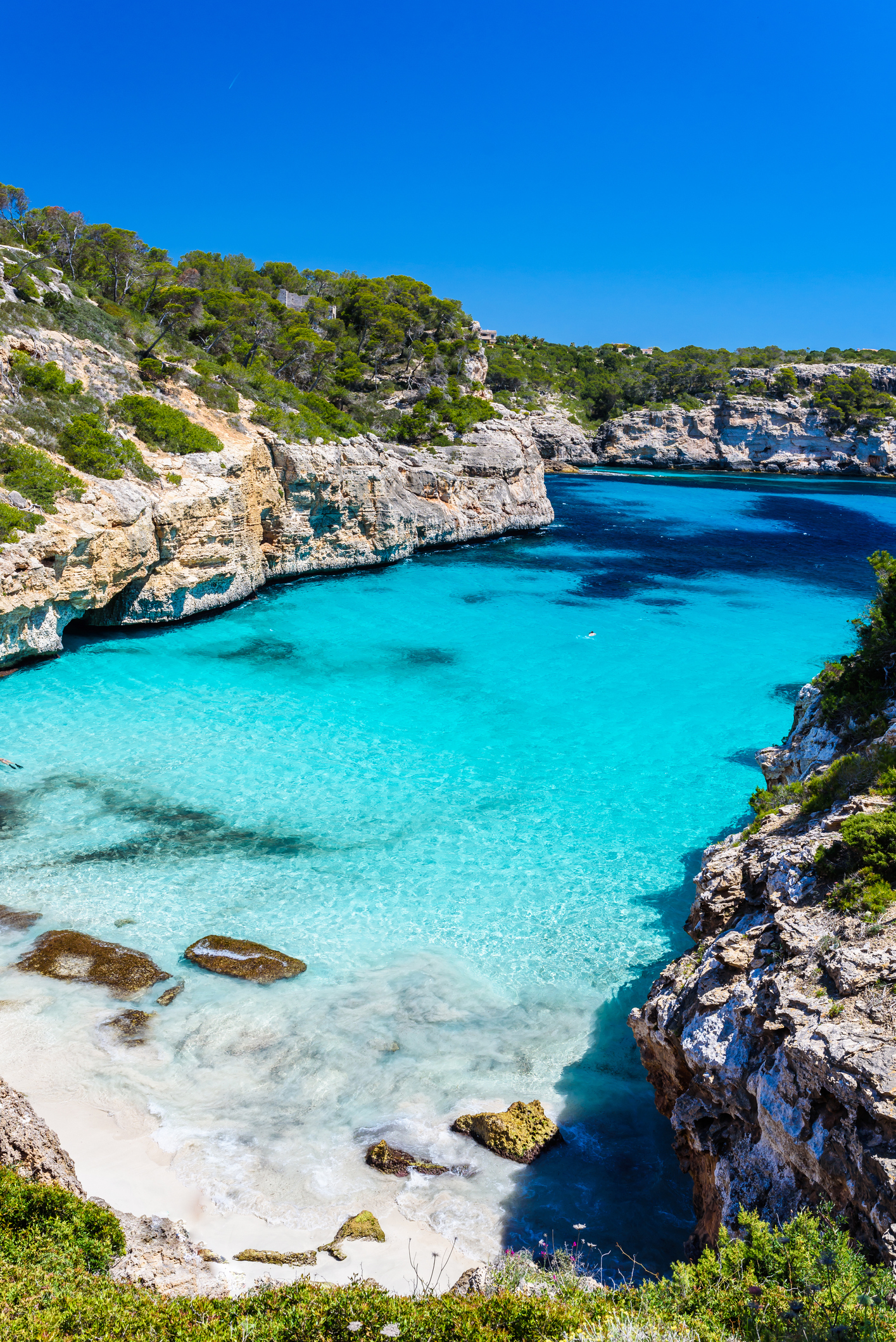 Cala turquesa en Mallorca entre acantilados rocosos y playa de arena.