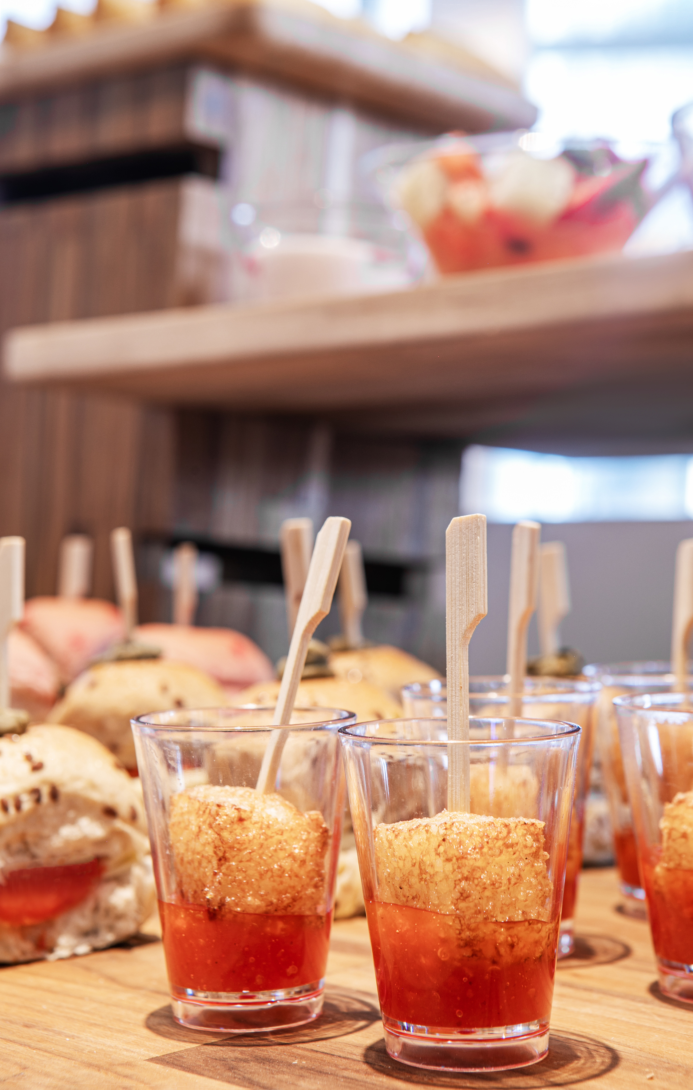 Appetizer cubes with red sauce in glasses, mini sandwiches at a buffet.