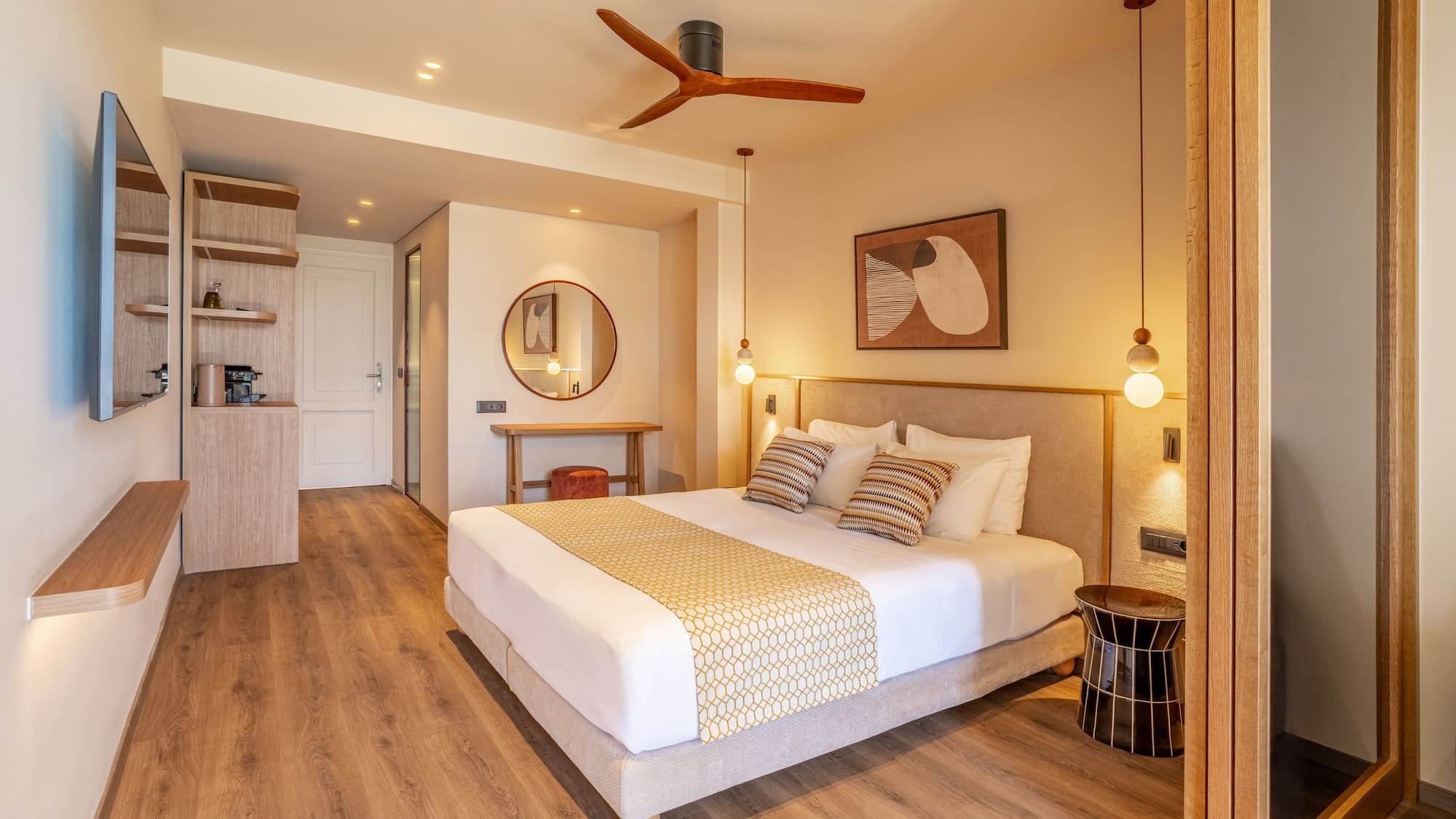 Modern hotel bedroom with king bed, wooden floor, beige walls, and ceiling fan.