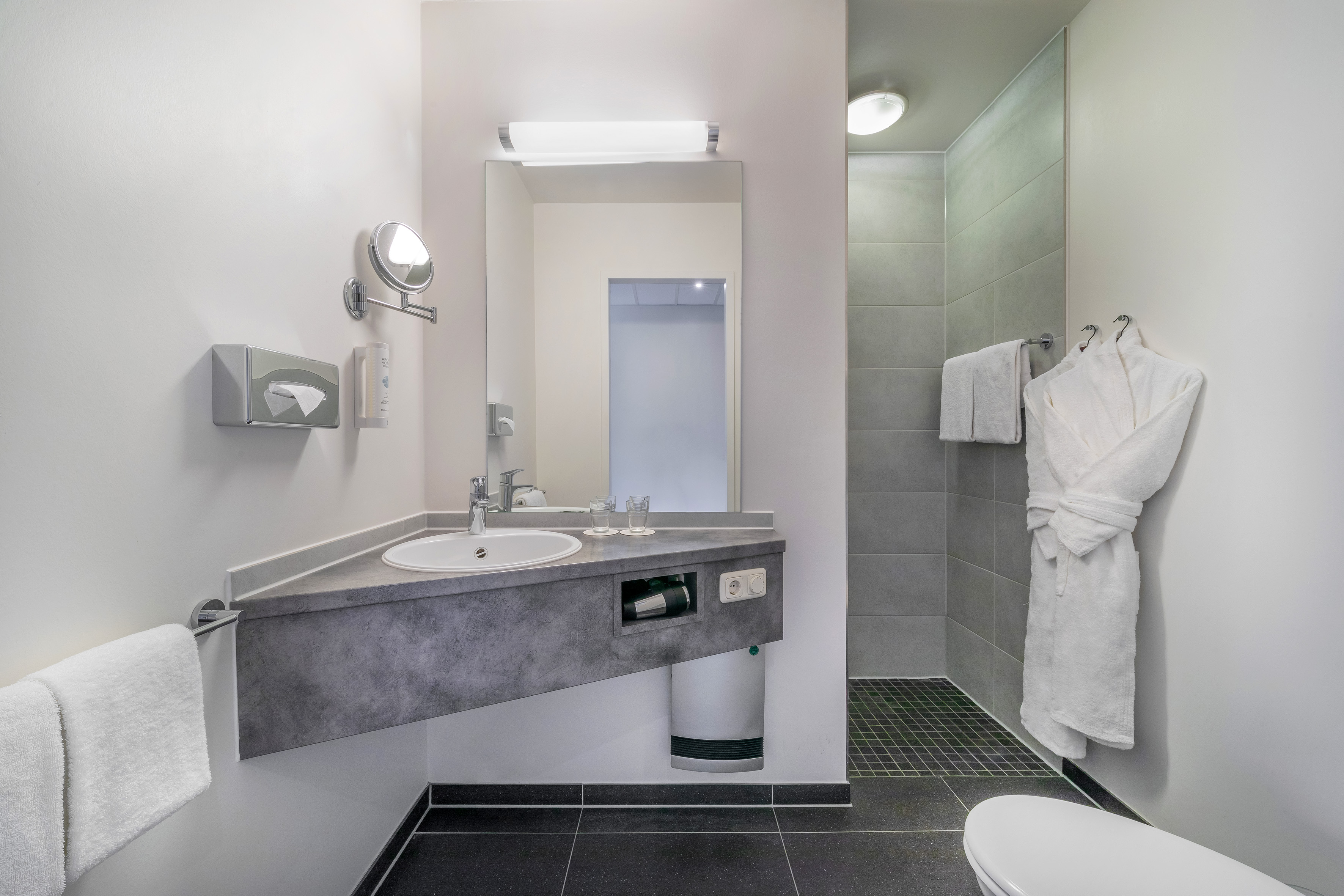Modern hotel bathroom with vanity, sink, mirror, shower, and toilet.