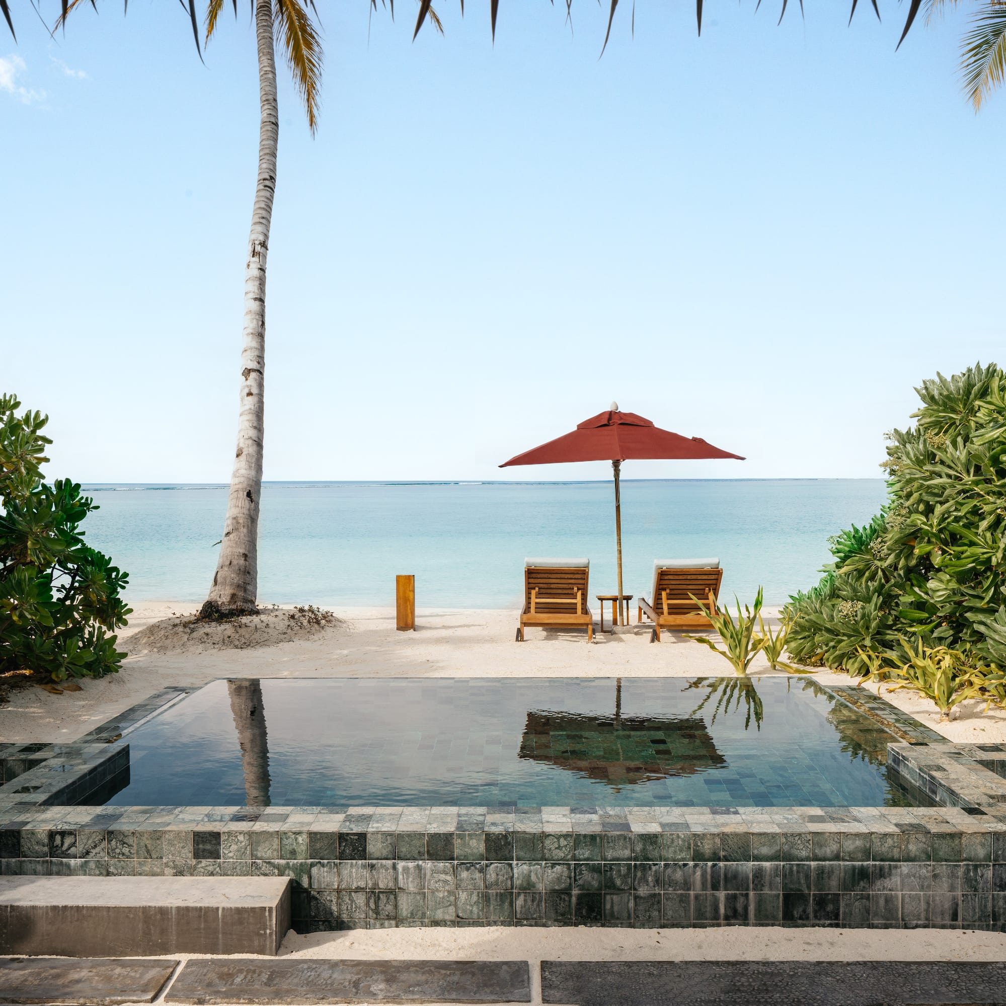 a pool with a deck chair and umbrella on a beach