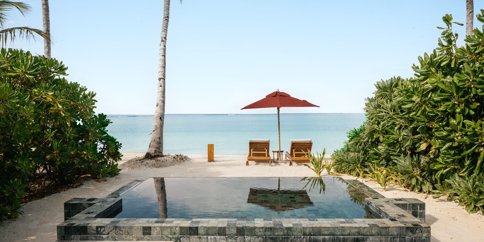 a pool with a deck chair and umbrella on a beach