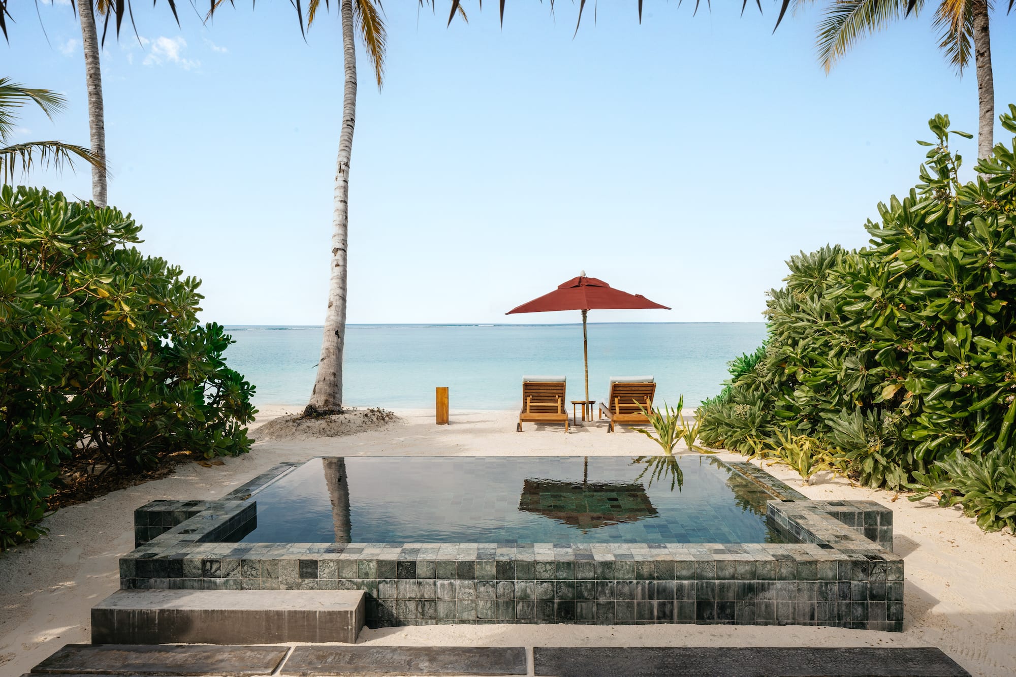 a pool with a deck chair and umbrella on a beach