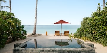 a pool with a deck chair and umbrella on a beach