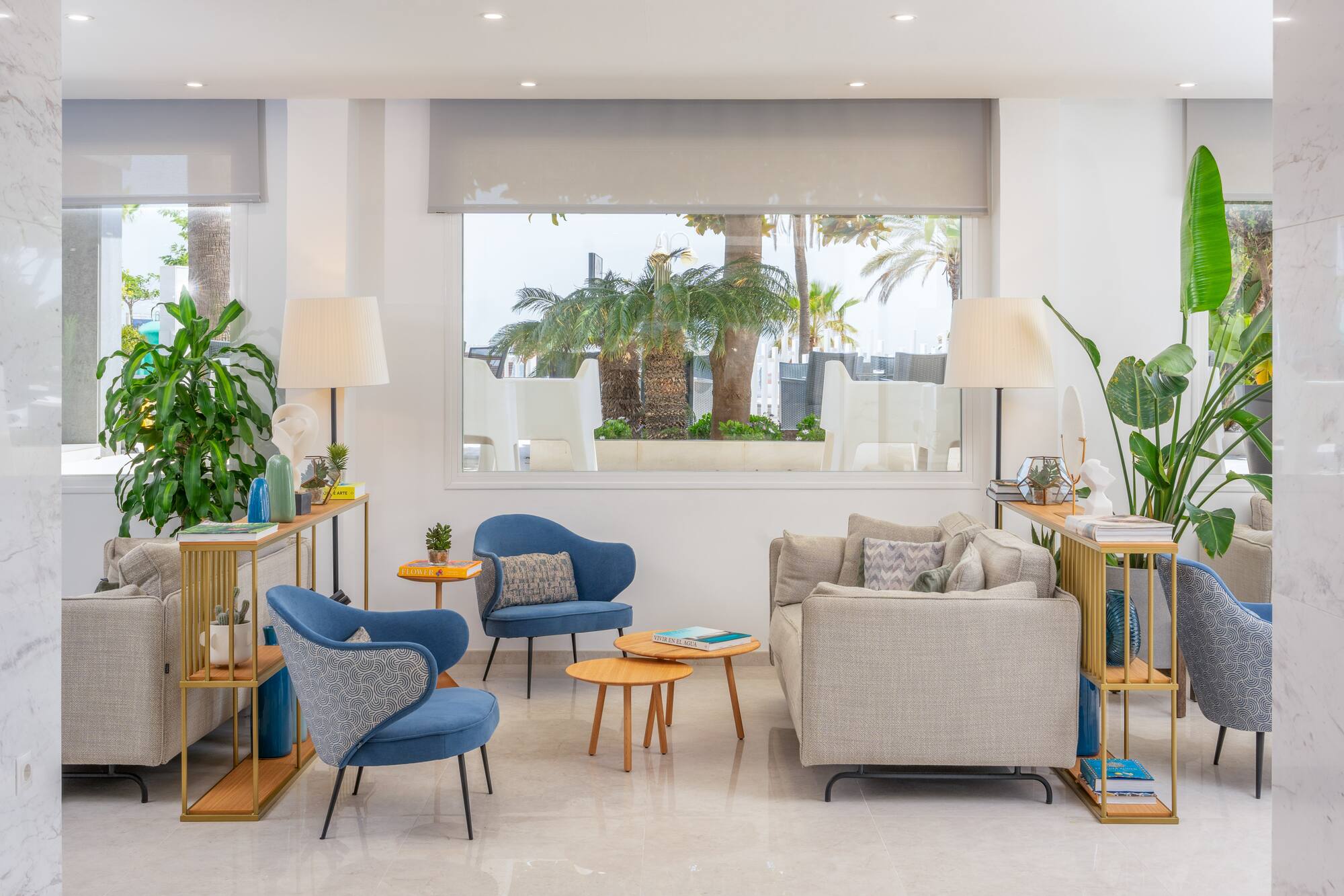 Modern resort lounge with blue armchairs, gray sofas, and palm tree view.