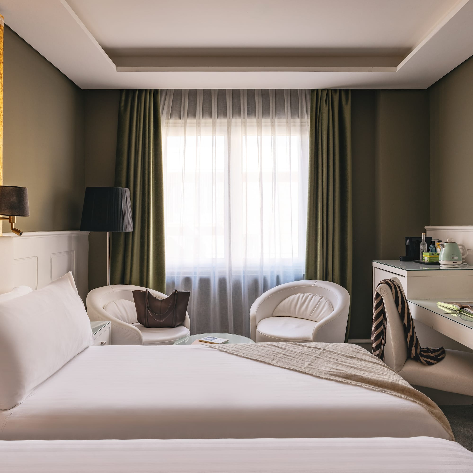 Suite de hotel de lujo: cama, escritorio, sillones blancos y pared dorada.