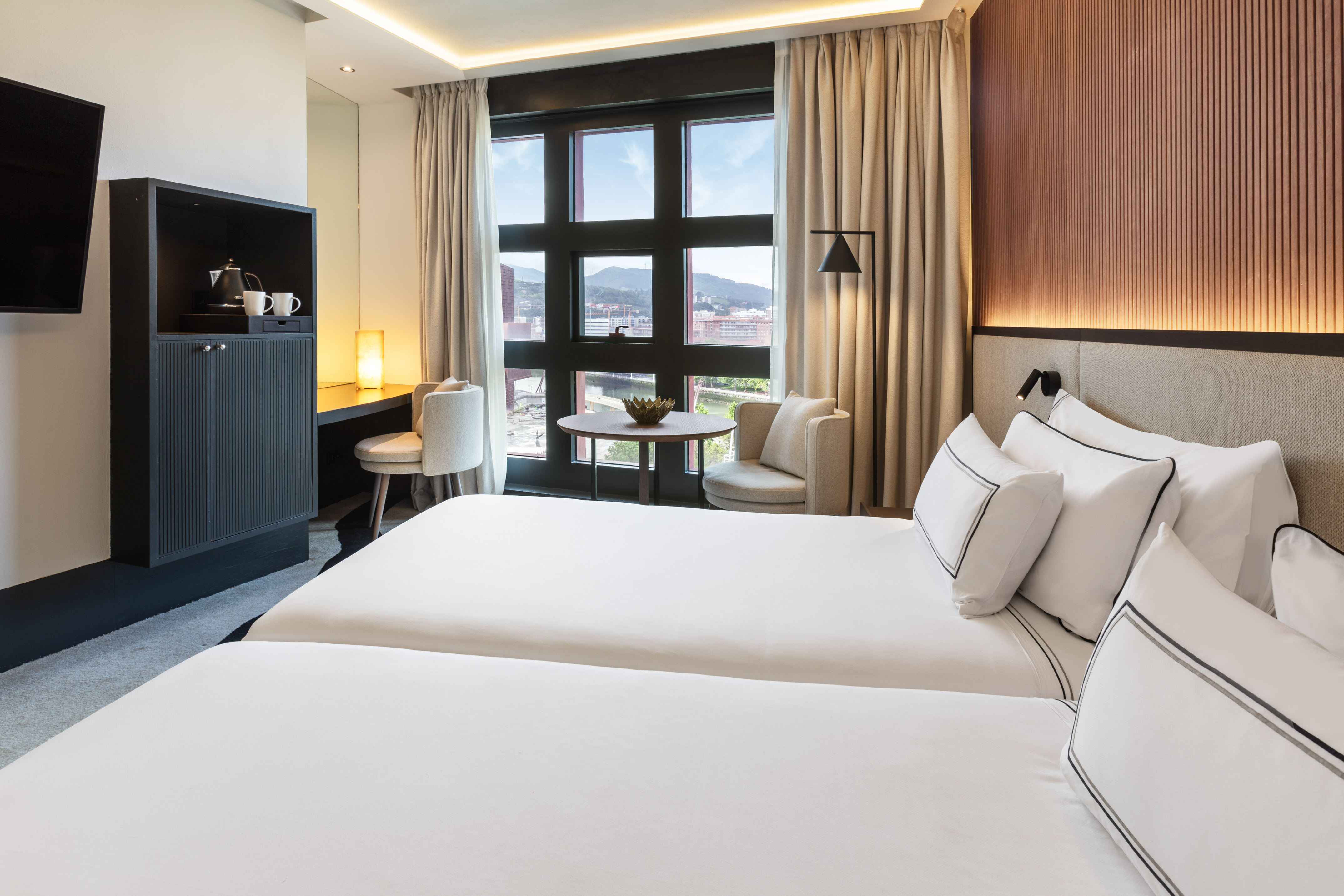 Spacious hotel room featuring twin beds, city views, and contemporary design.