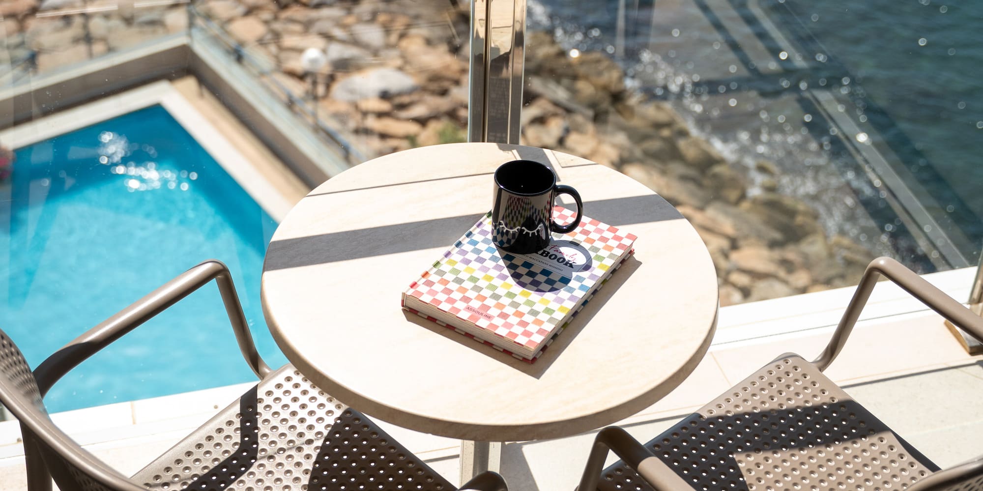 a table with chairs and a book on a balcony overlooking the ocean