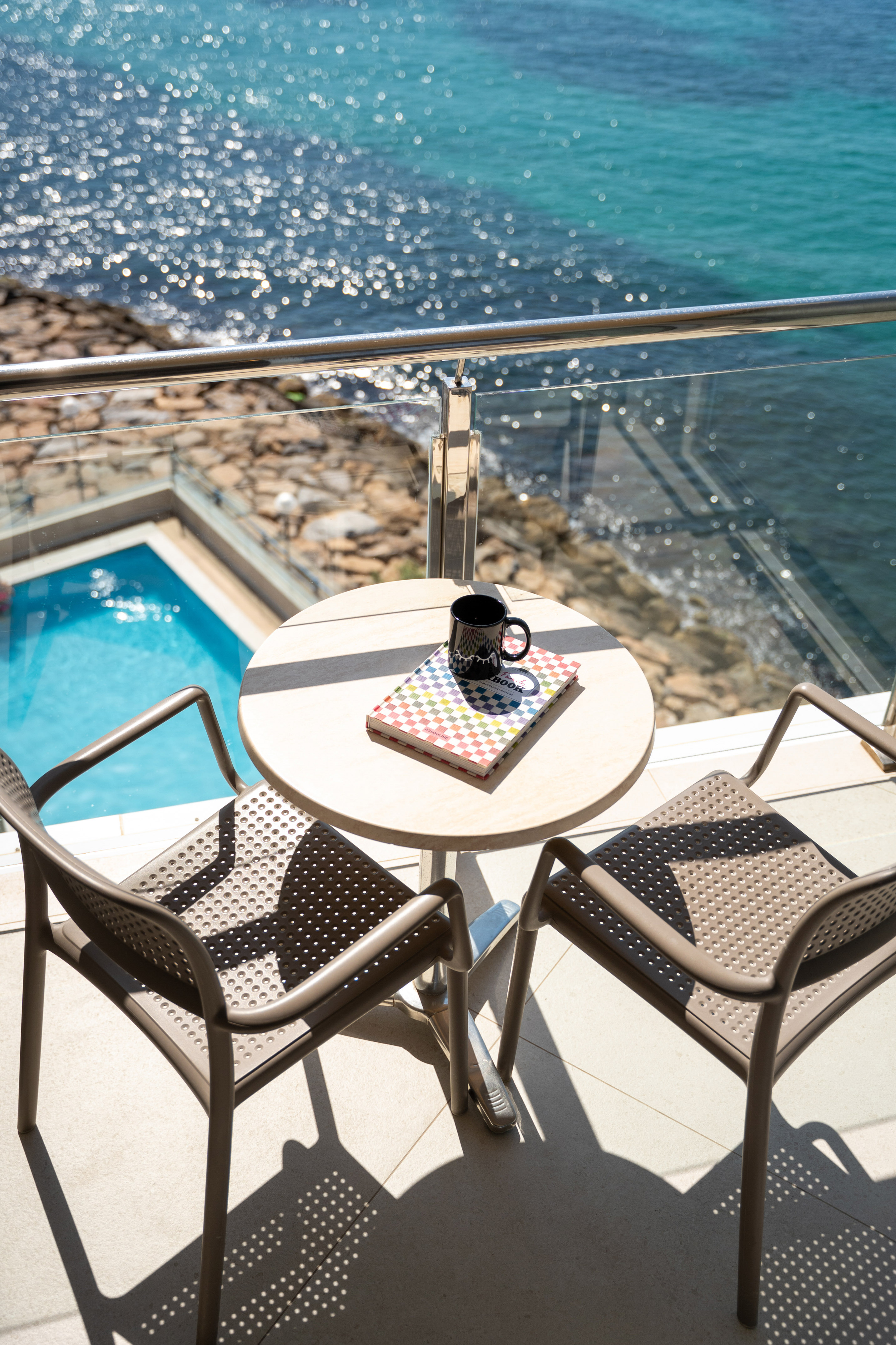 Balcony with ocean view and pool, table with coffee cup and book.