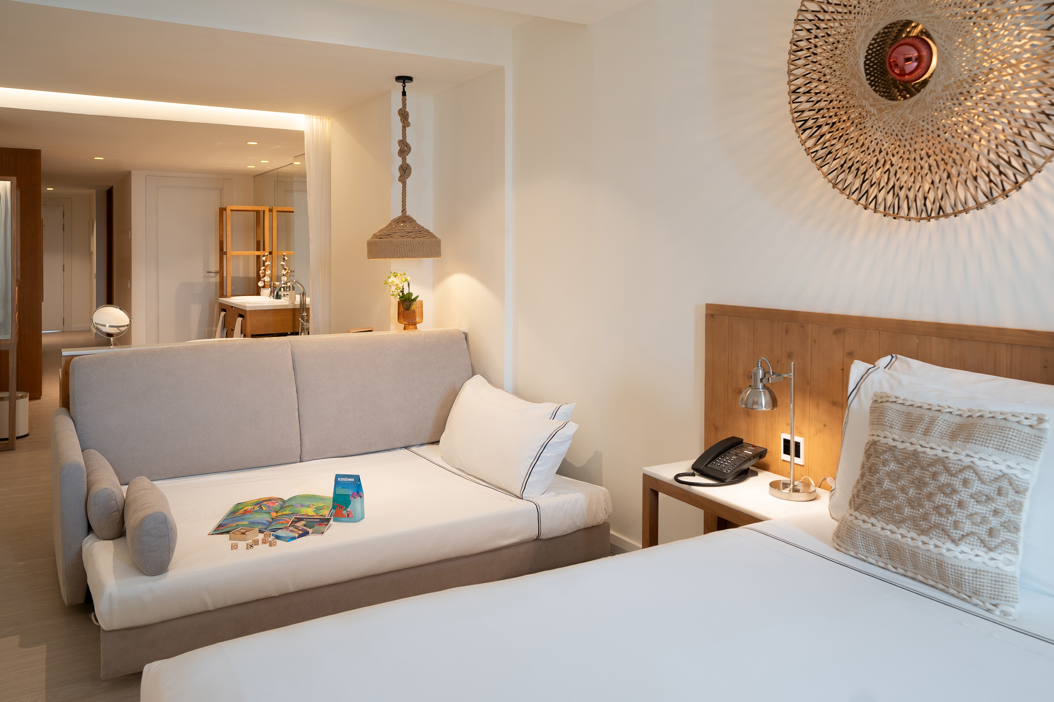 Modern hotel room with bed, daybed, and natural woven decor.