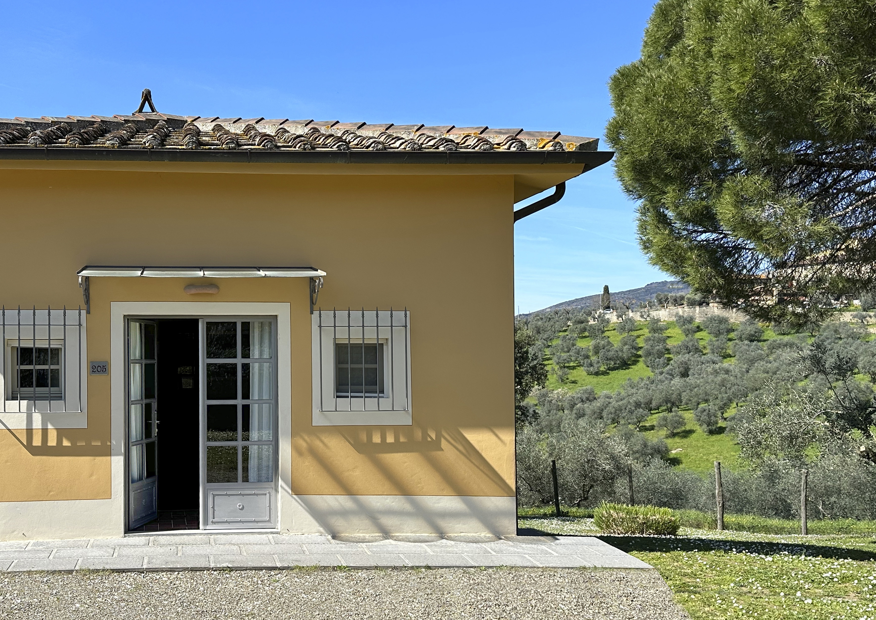 Sunny yellow Tuscan villa with open door, terracotta roof, and olive groves.