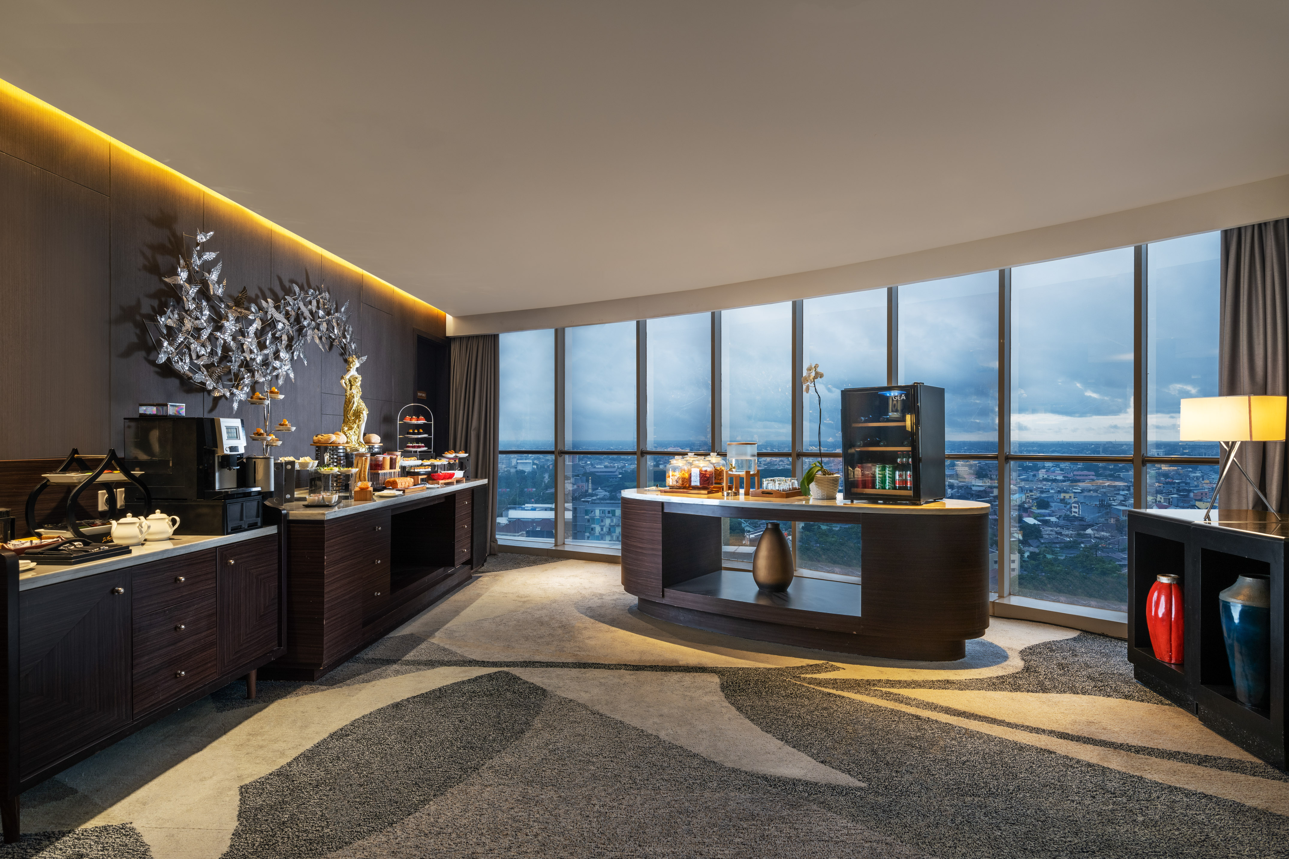 Modern hotel lounge buffet with expansive city view and refreshments.